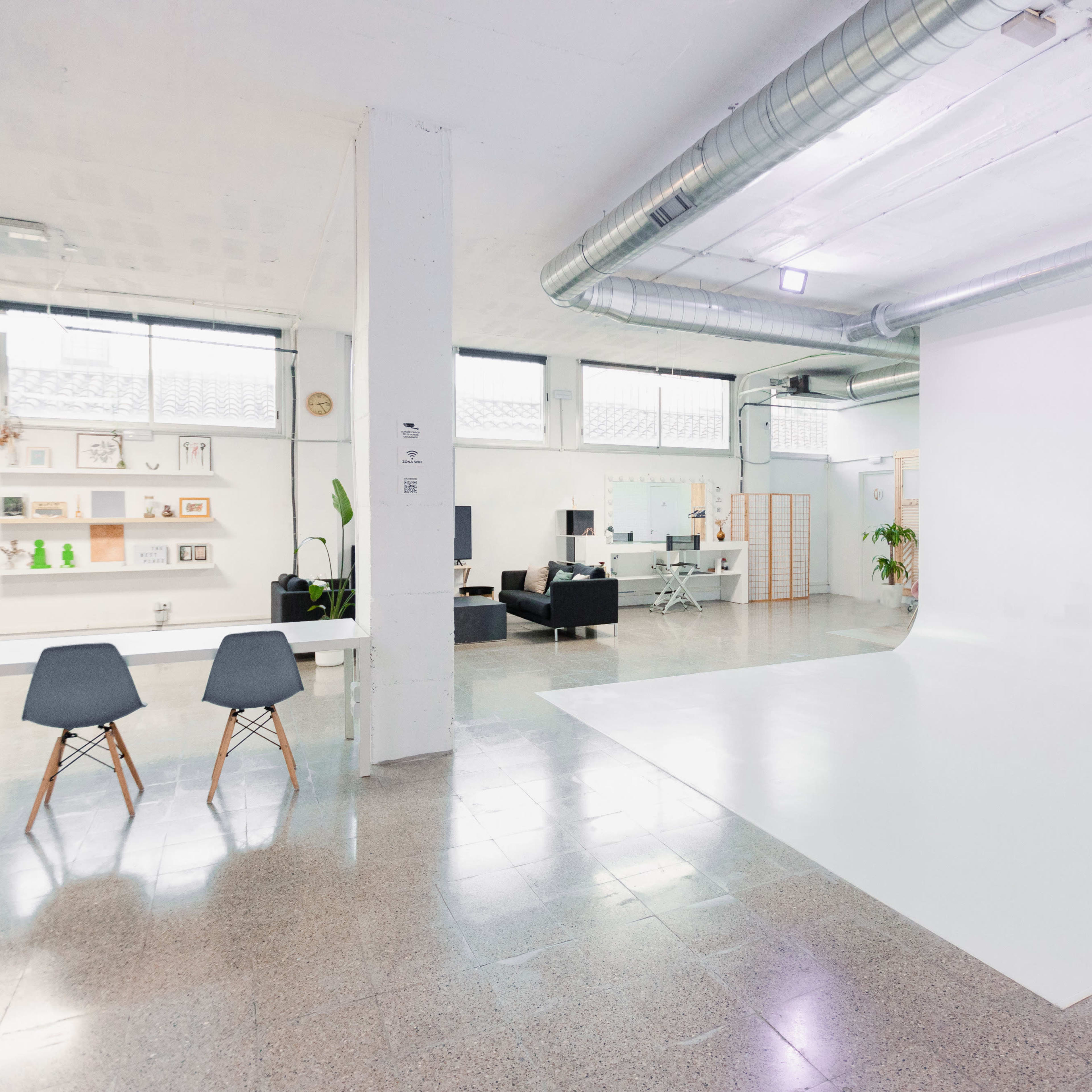 A spacious, modern studio with a white backdrop, a table with chairs, and a seating area.