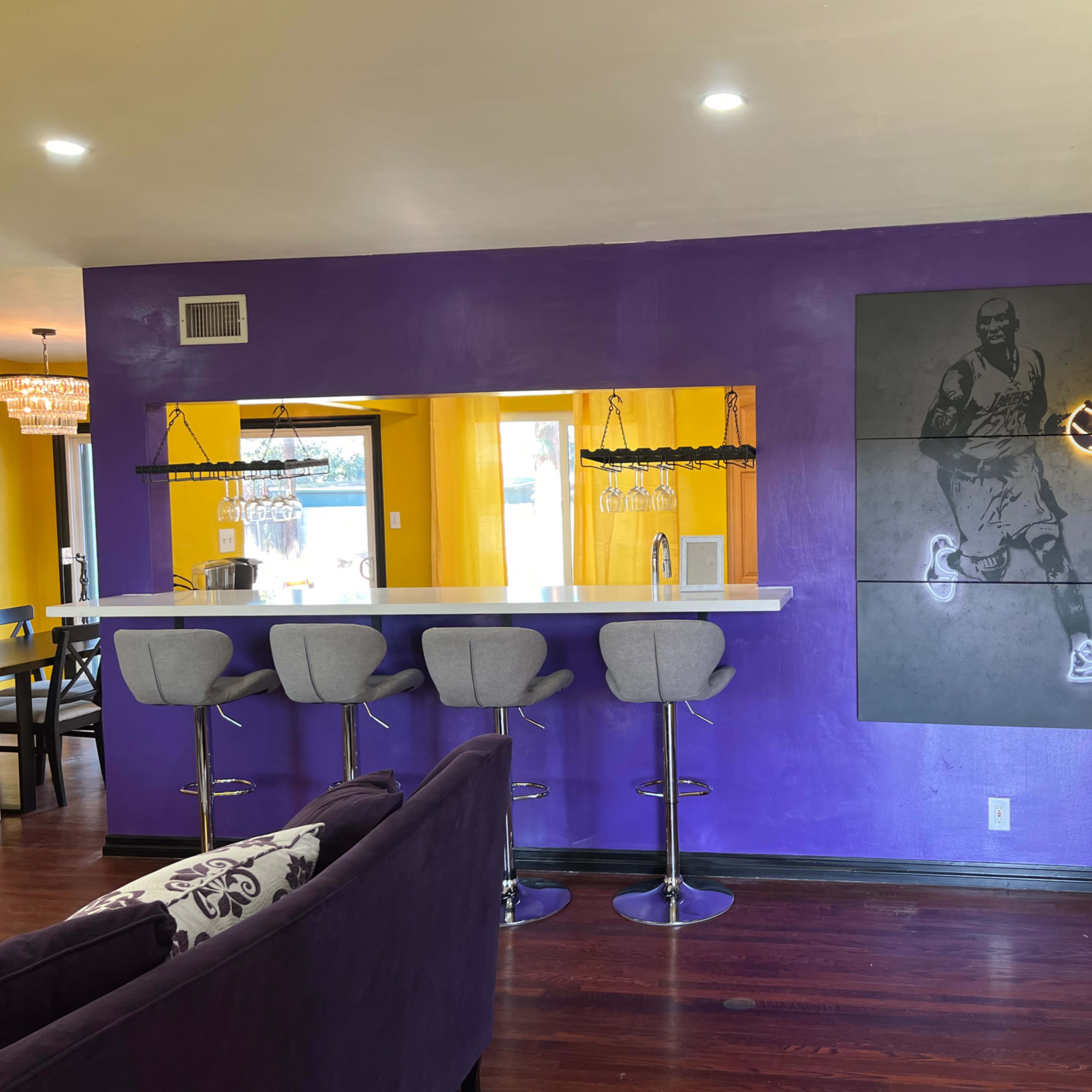 A brightly colored room with purple and yellow walls, a bar with gray stools, and a basketball-themed artwork on the wall.