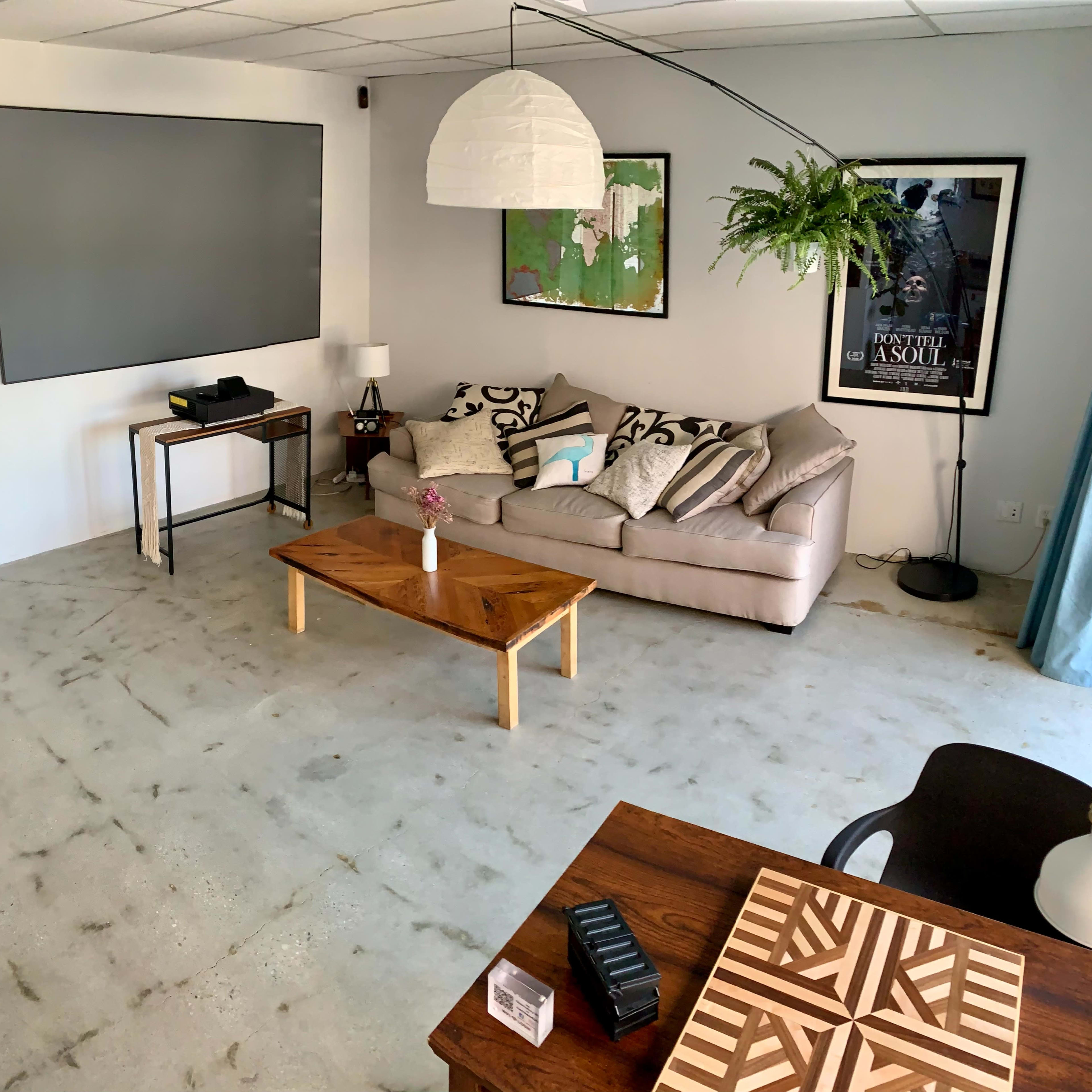 A modern, minimalistic living space with a gray wall, a comfortable sofa, a wooden coffee table, and a large pendant light.