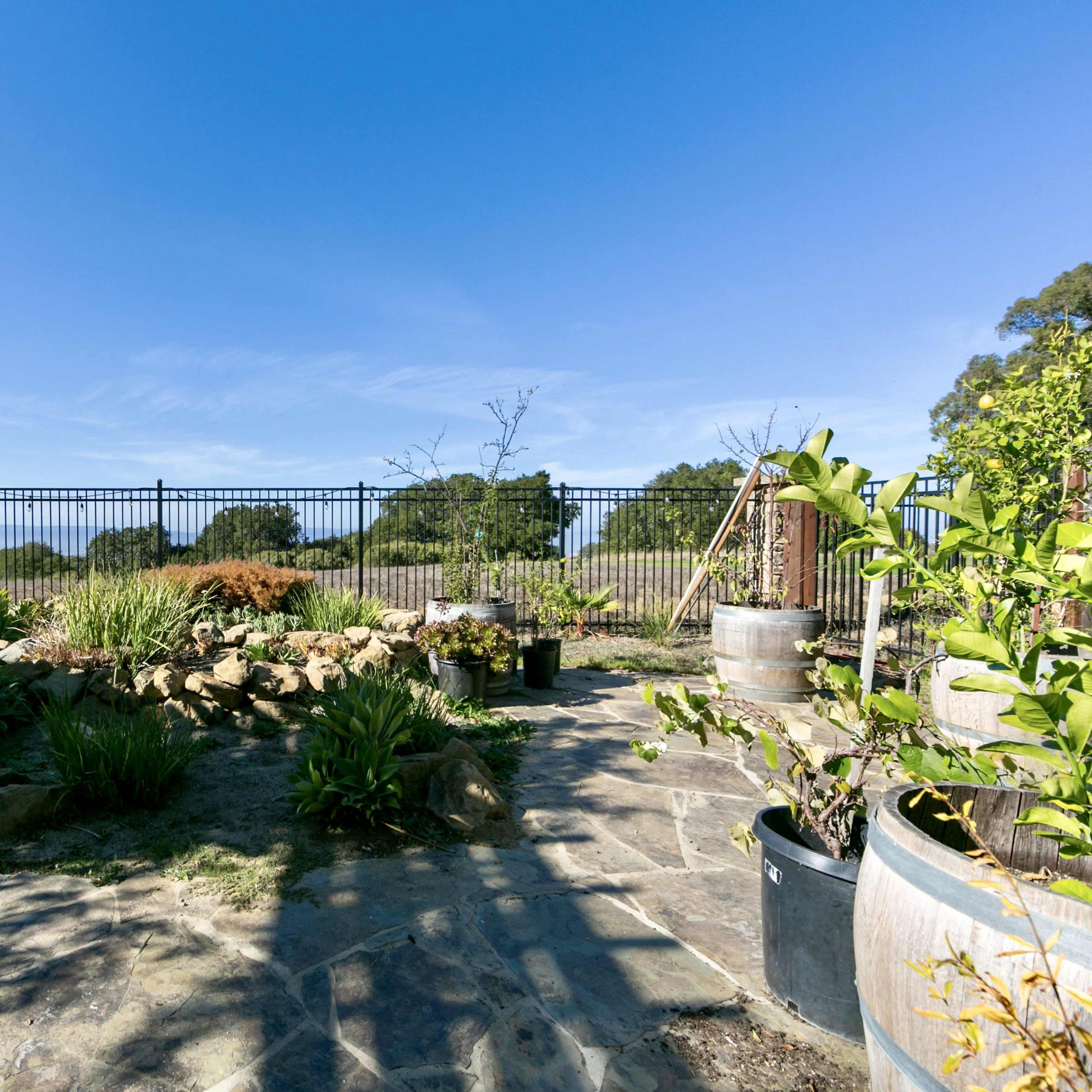A landscaped garden area features stone pathways, containers with plants, and a fence enclosing a scenic view.
