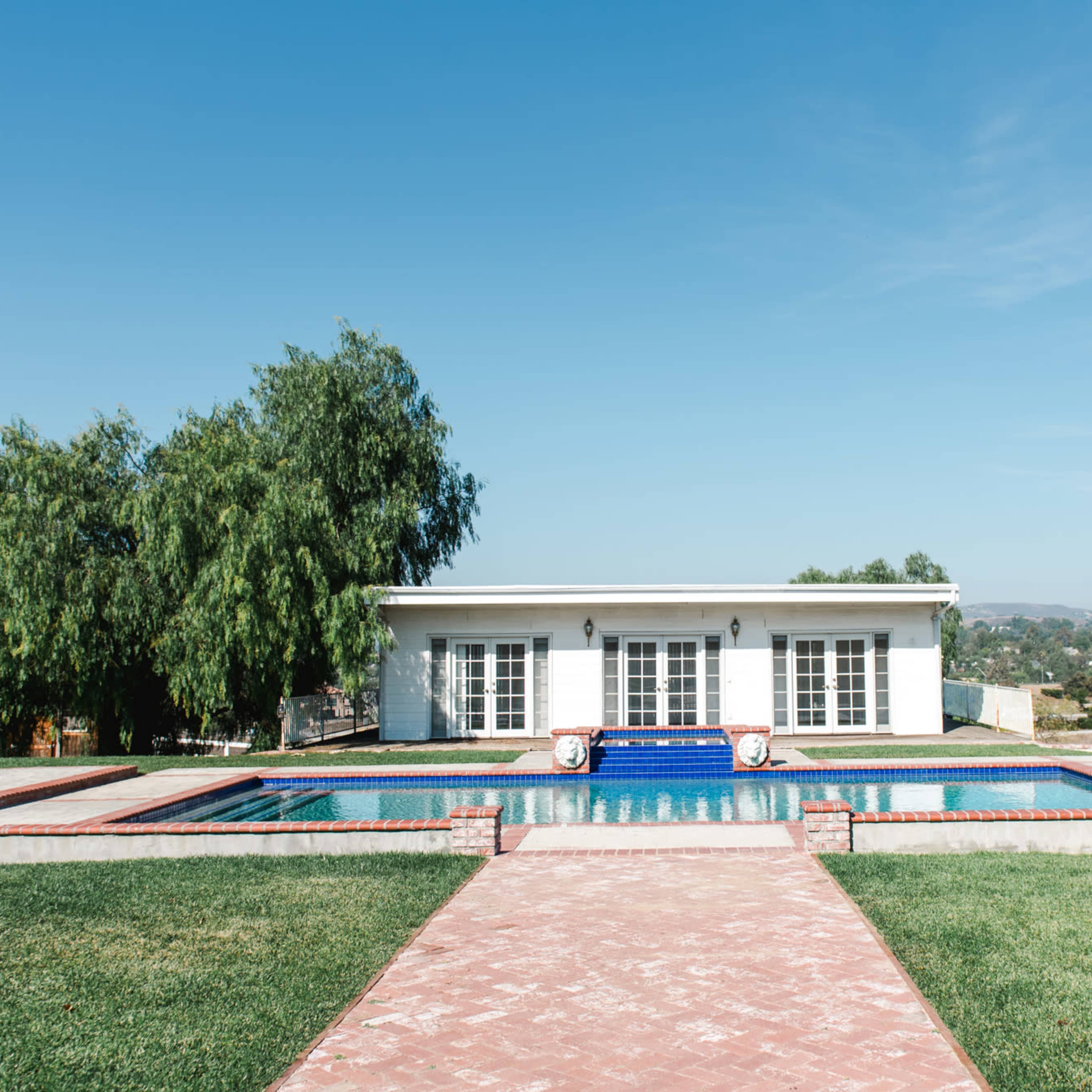 A modern house with a blue swimming pool and landscaped gardens is set against a clear sky.