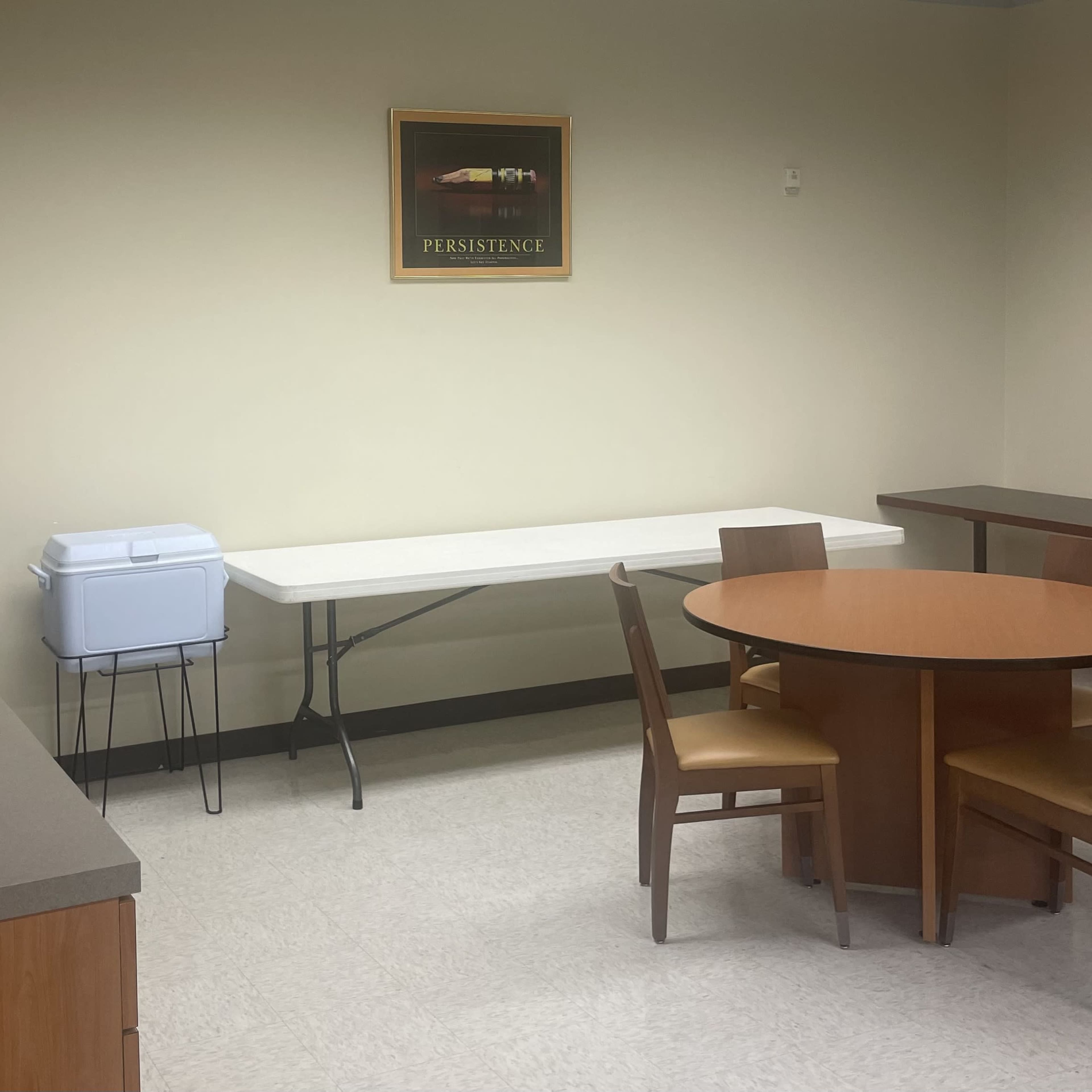 A small kitchen area with a sink, a cooler on a table, and a round dining table surrounded by four chairs.