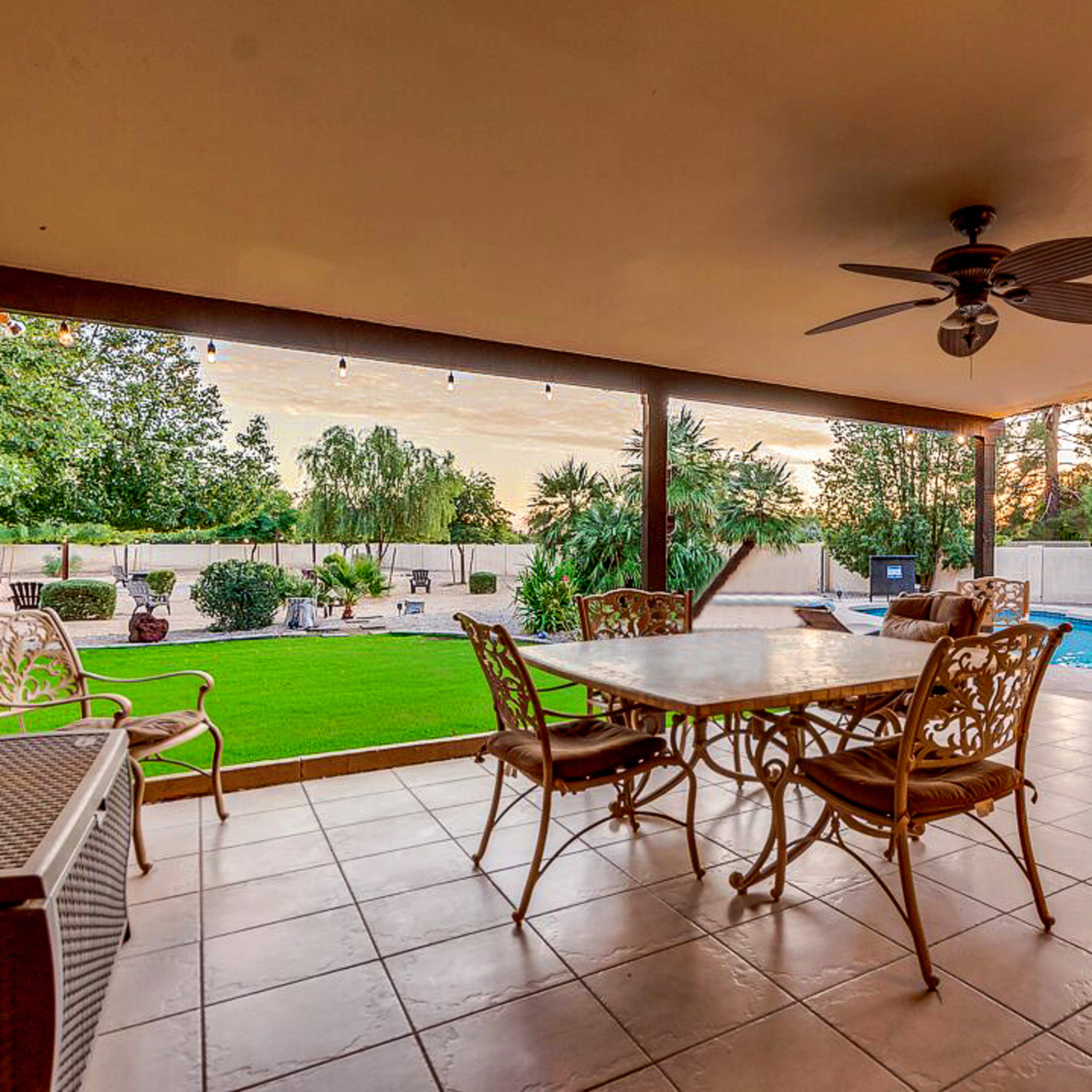 A patio area features a table and chairs overlooking a landscaped yard with a swimming pool.