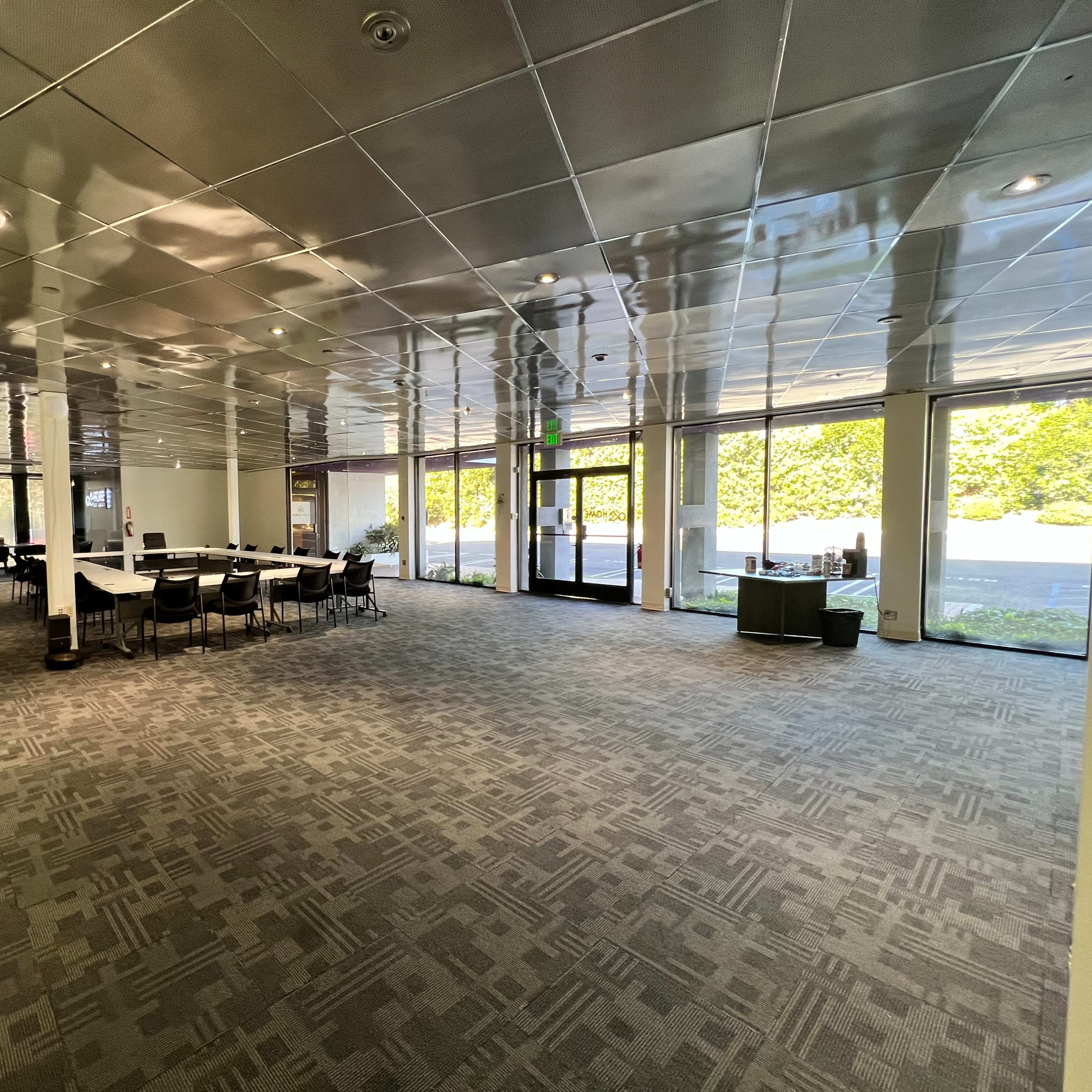 A modern, spacious interior of a building with a seating area arranged around a central table and large windows providing natural light.