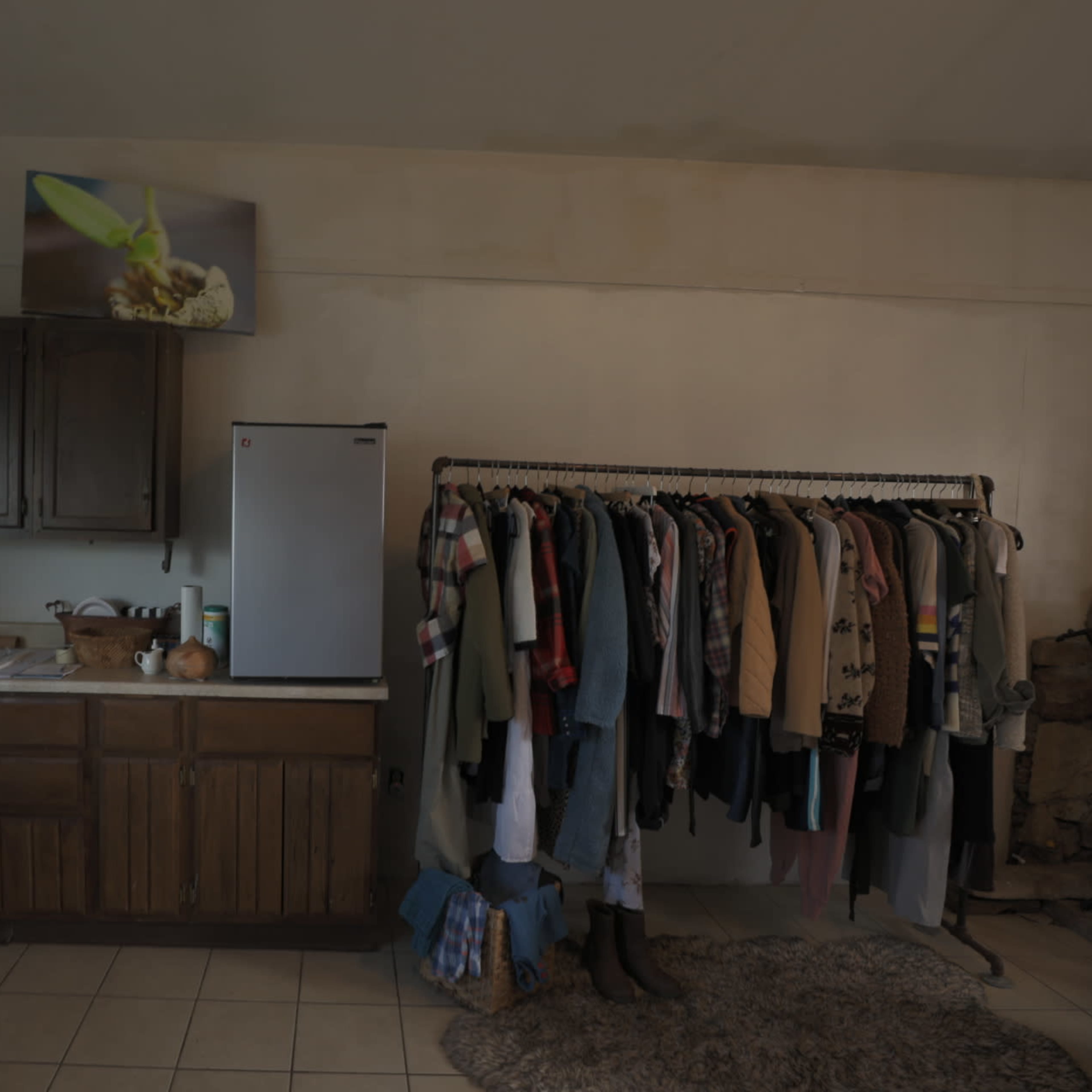A kitchen area with wooden cabinets, a refrigerator, and a clothing rack filled with various garments.