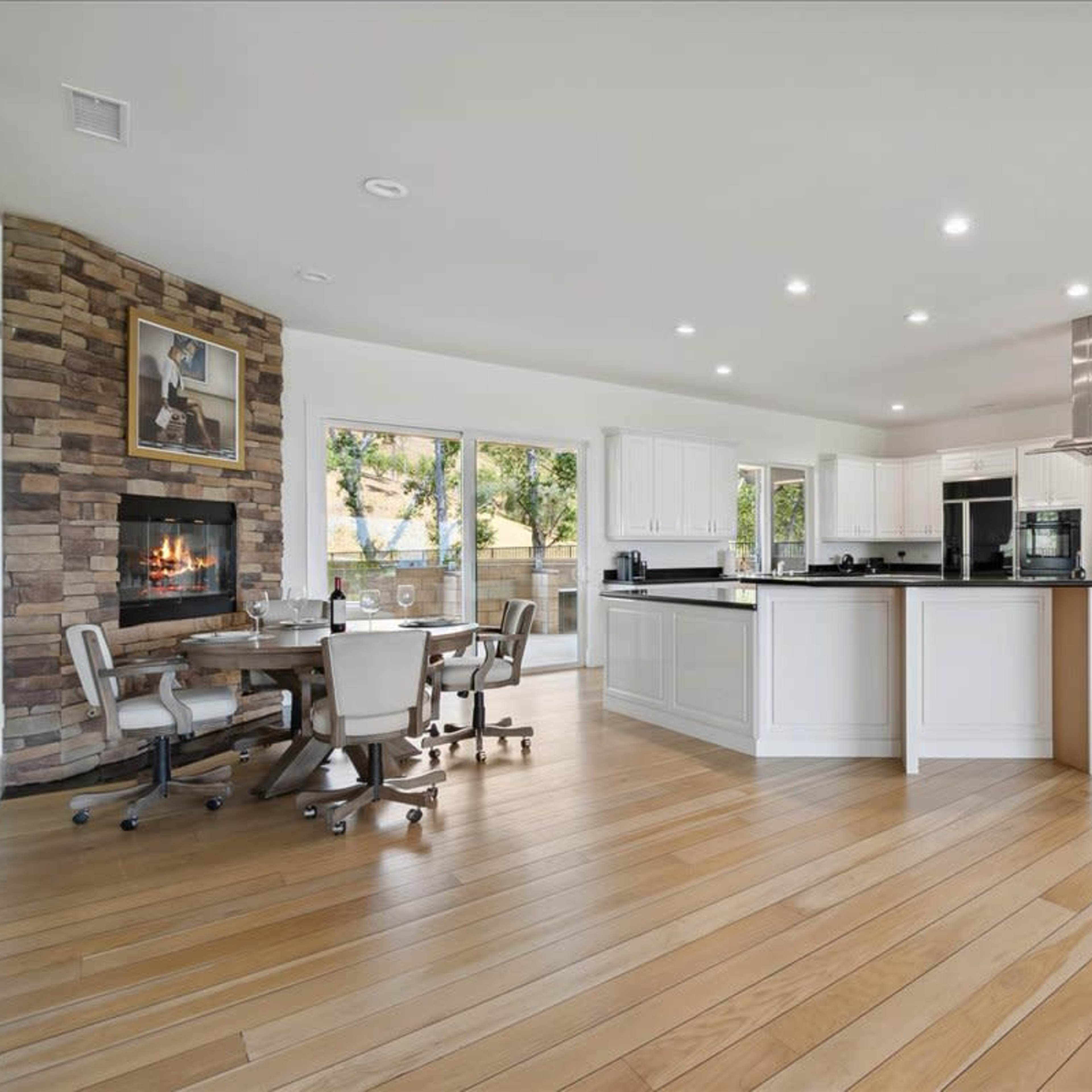A modern kitchen with white cabinetry, a stone feature wall with a fireplace, and a dining area with a round table and chairs.
