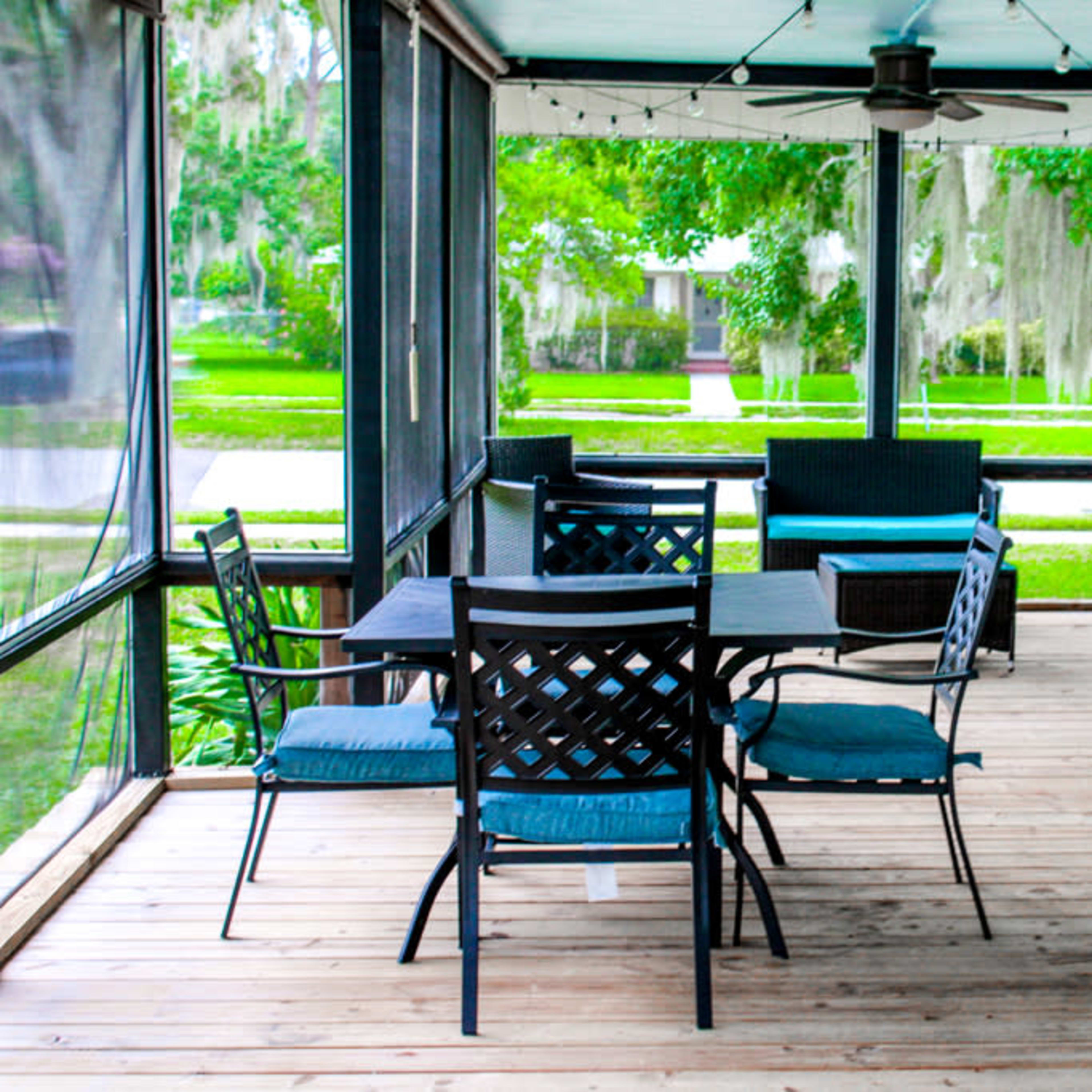A screened porch featuring a wooden floor, a dining table with chairs, a seating area, and a charcoal grill.