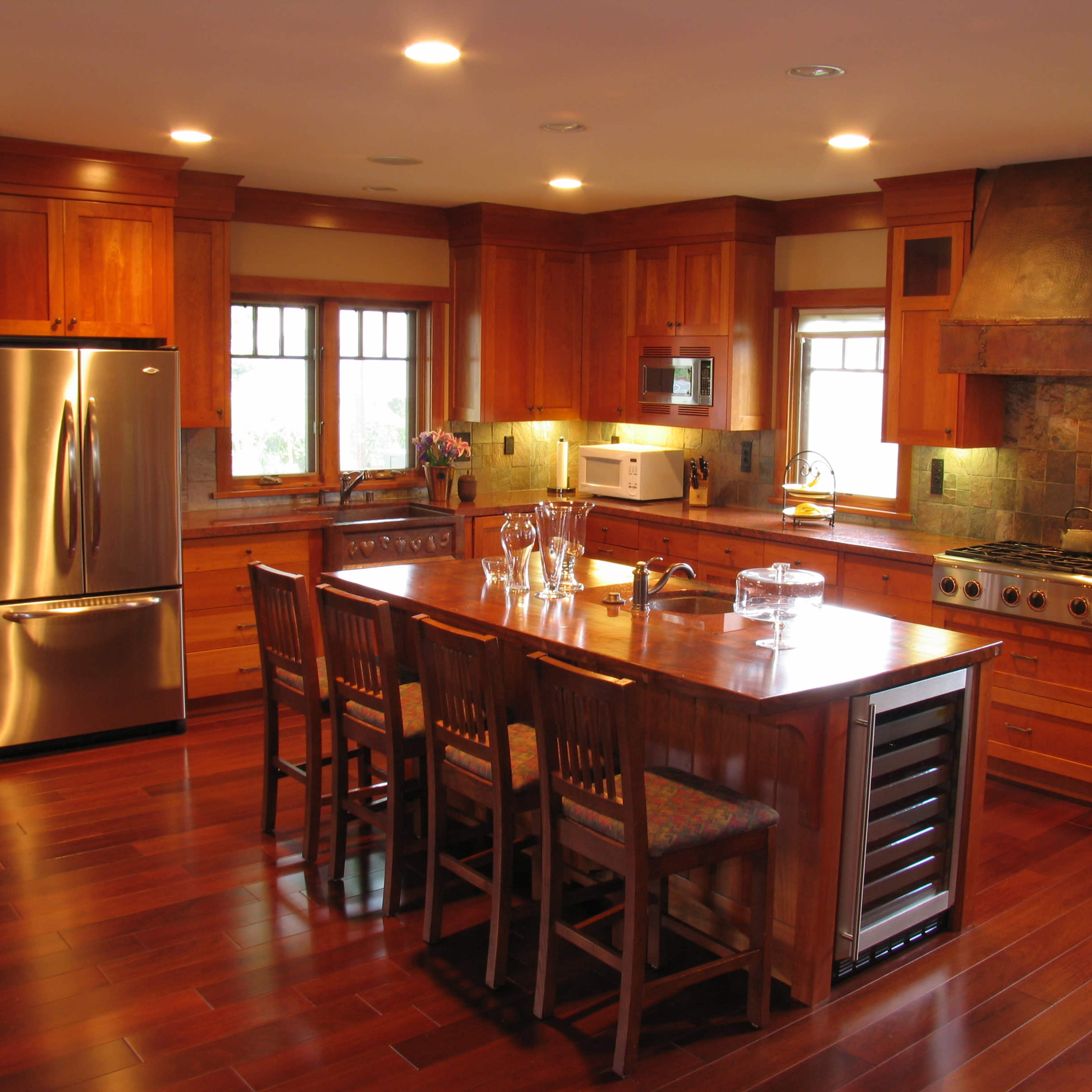 The kitchen features wooden cabinetry, a central island with seating for six, stainless steel appliances, and a stone backsplash.