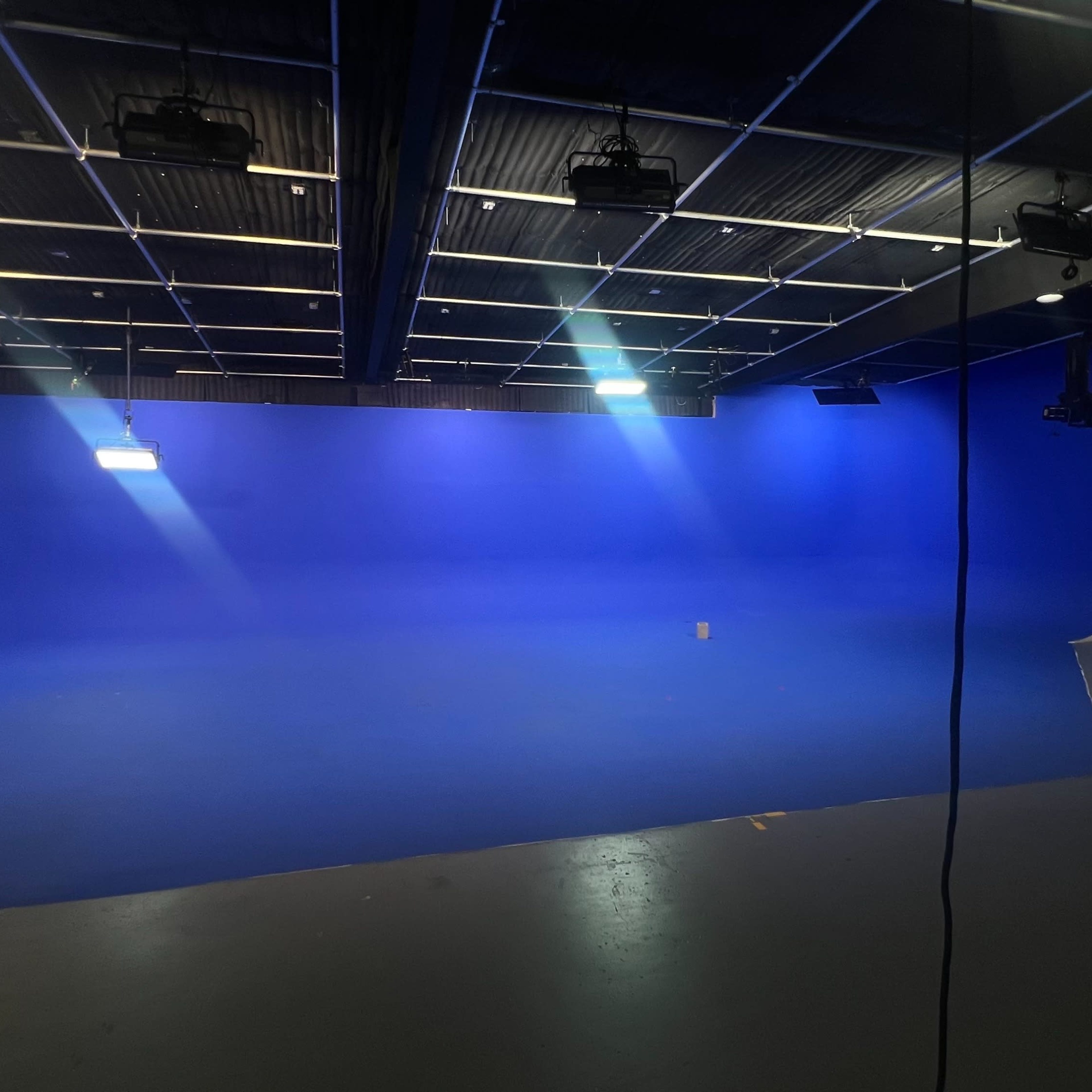 A studio with a blue backdrop, equipped with lighting and cameras, is set up for a recording or production.