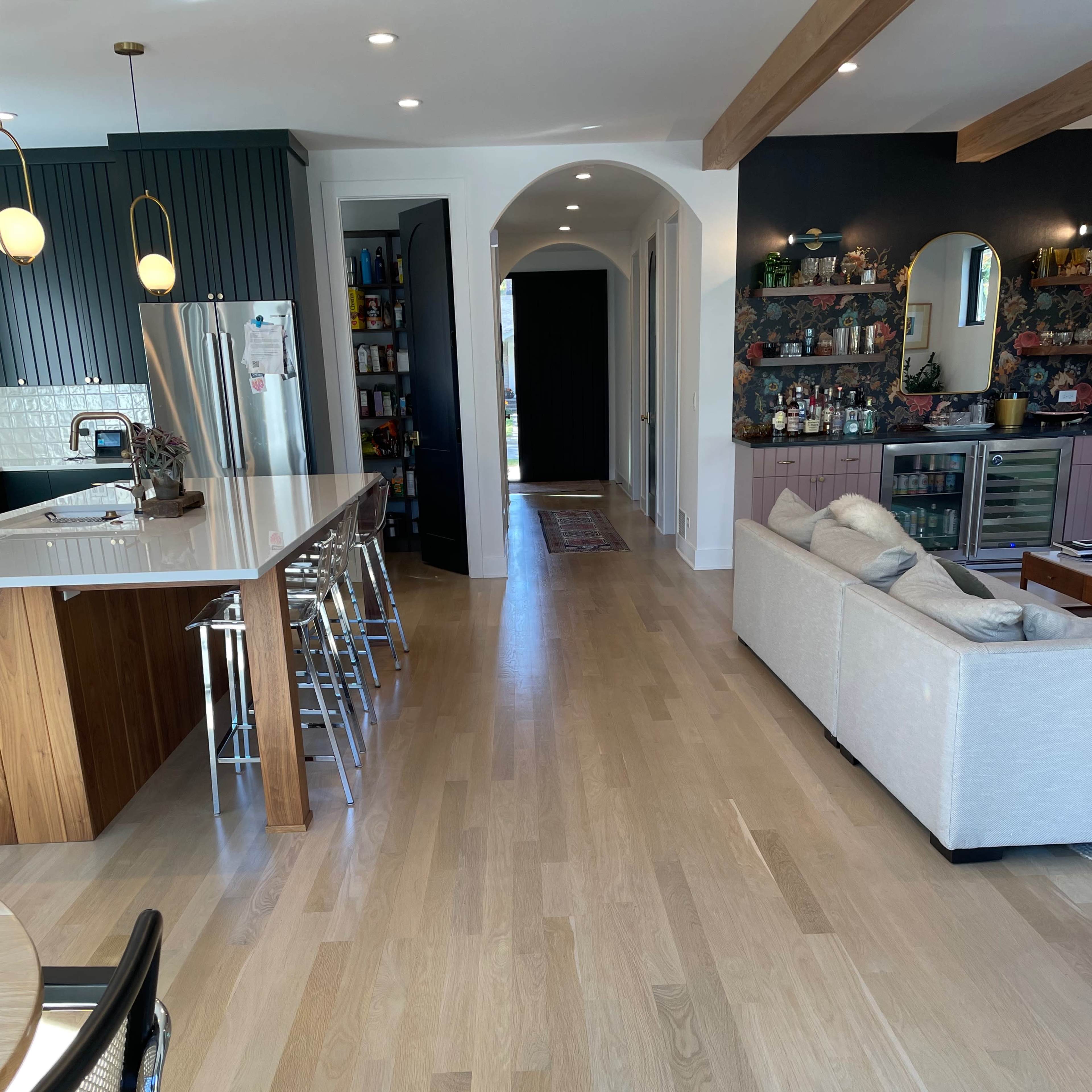 An open-concept living space featuring a kitchen with a large island and bar stools, a hallway leading to another room, and a cozy seating area with a light-colored sofa.