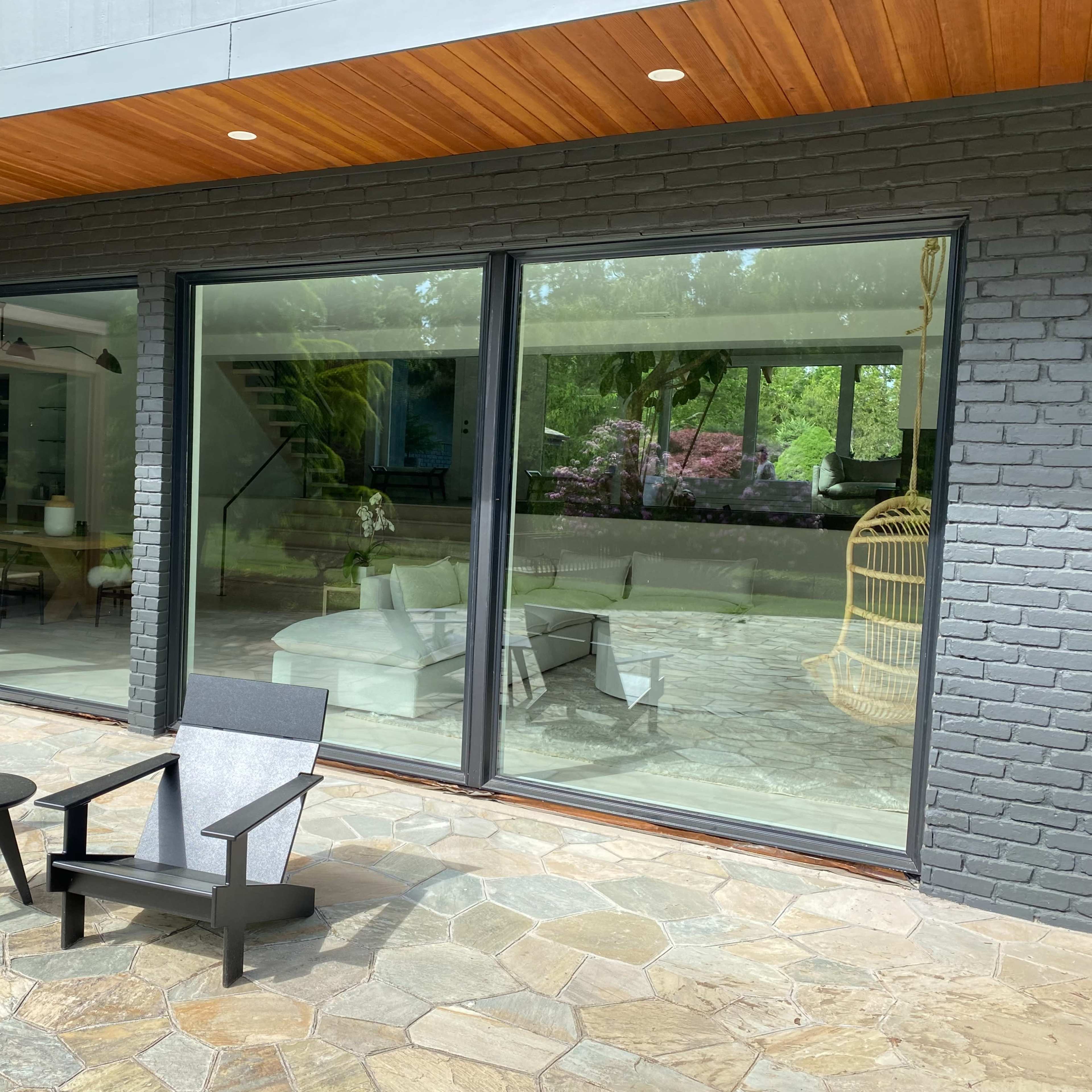 A patio area features two black chairs and a small table in front of large glass windows reflecting an interior space.