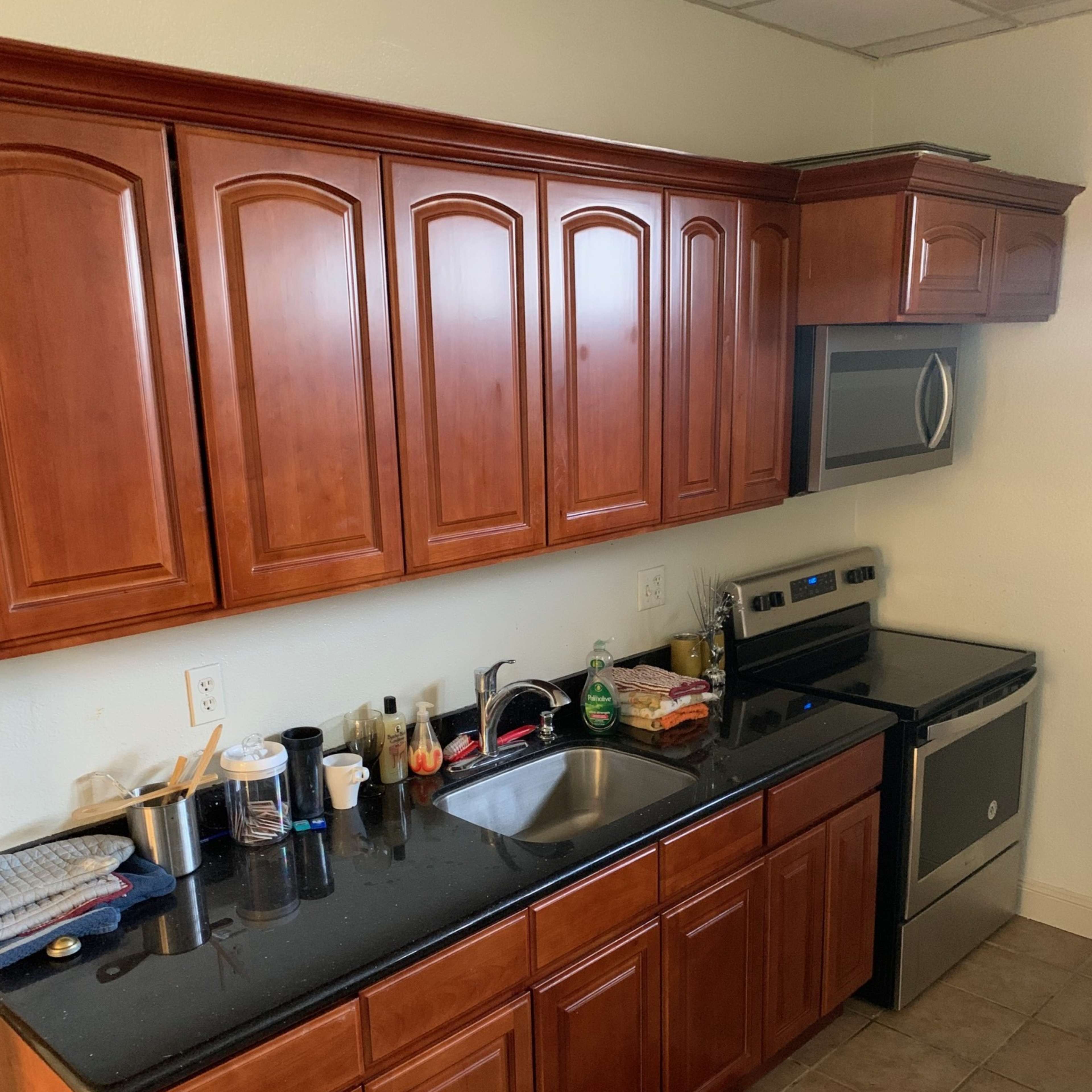 A kitchen with wooden cabinets, a stainless steel stove and microwave, a sink, and various items on the counter.