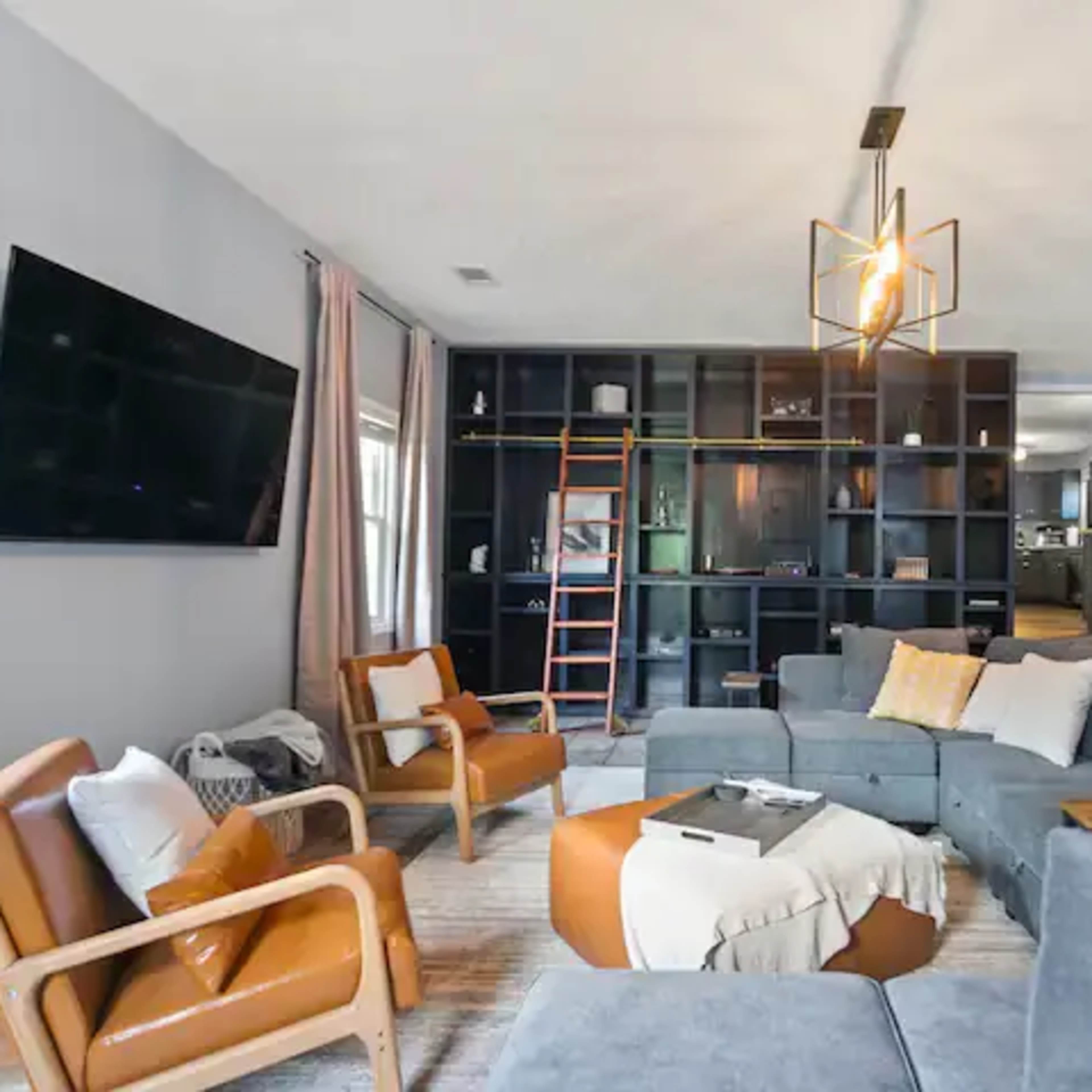 The living room features a sectional sofa, two armchairs, a coffee table, and a large wall-mounted television against a backdrop of built-in shelves.