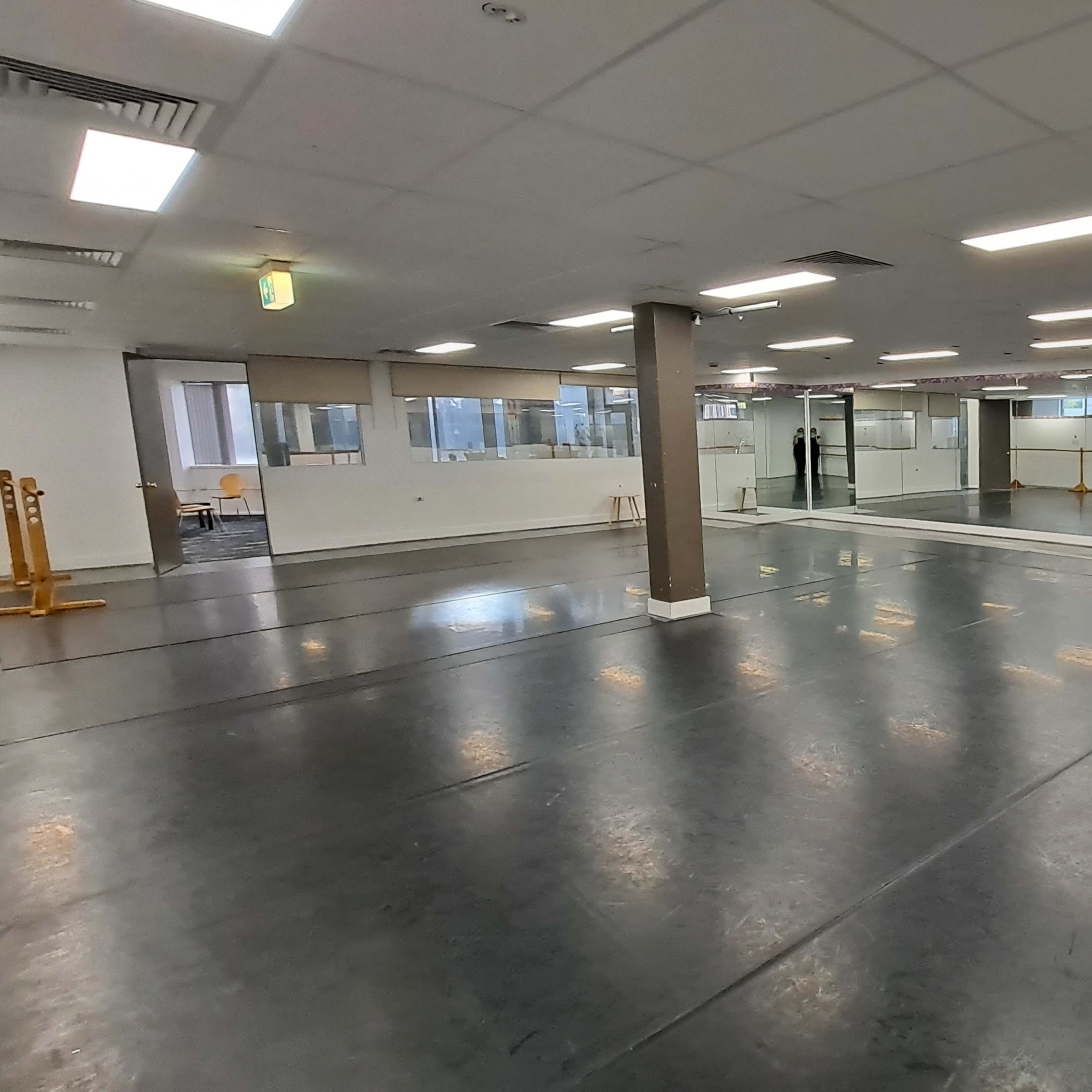 A large, empty dance studio with mirrors along two walls and wooden ballet barres positioned on both sides.