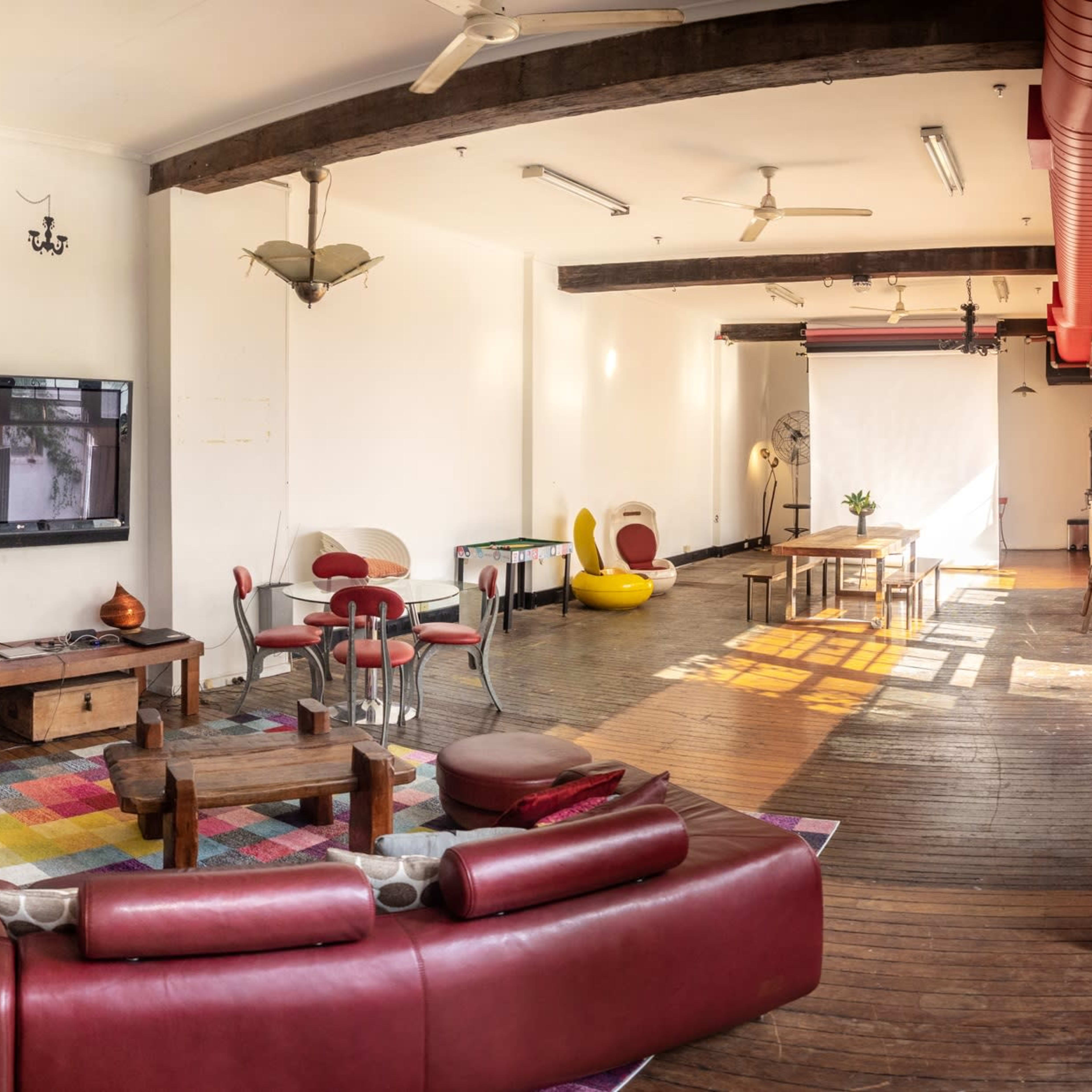 A spacious, well-lit living area with wooden floors, a large red couch, a television, and various seating arrangements.