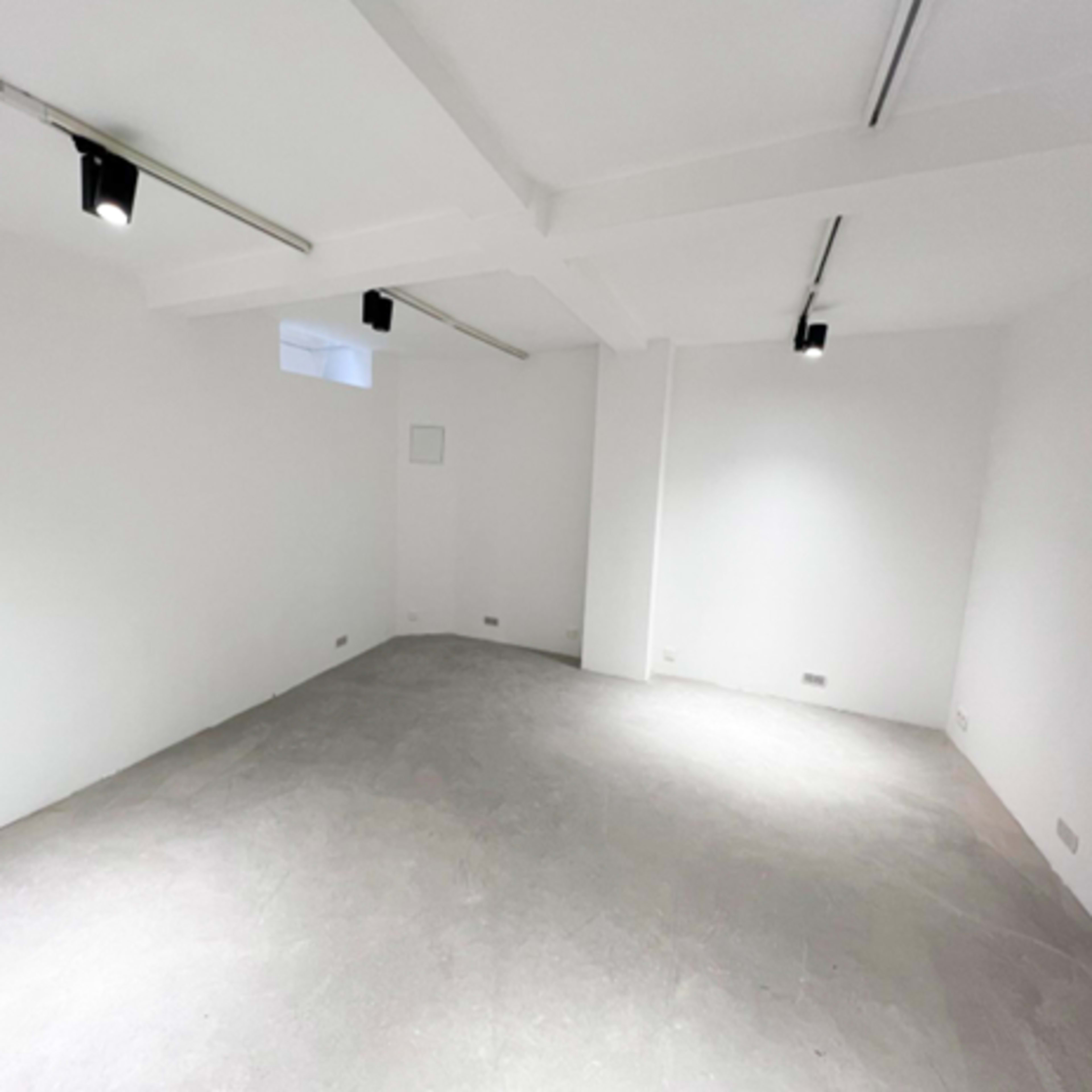 A bare white room with concrete flooring and overhead lights.