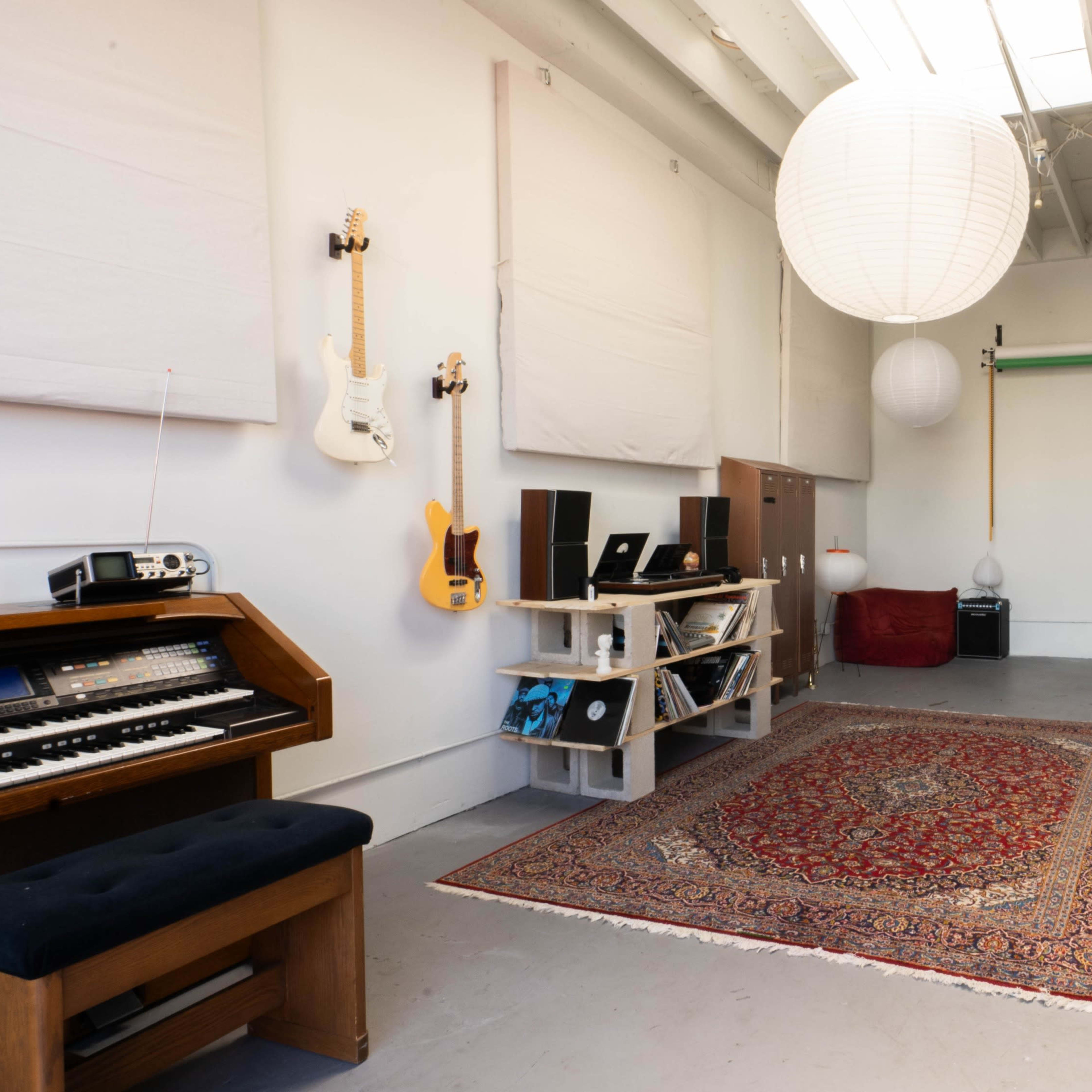 A spacious music studio with a wooden keyboard, a patterned rug, and various lighting fixtures hanging from the ceiling.