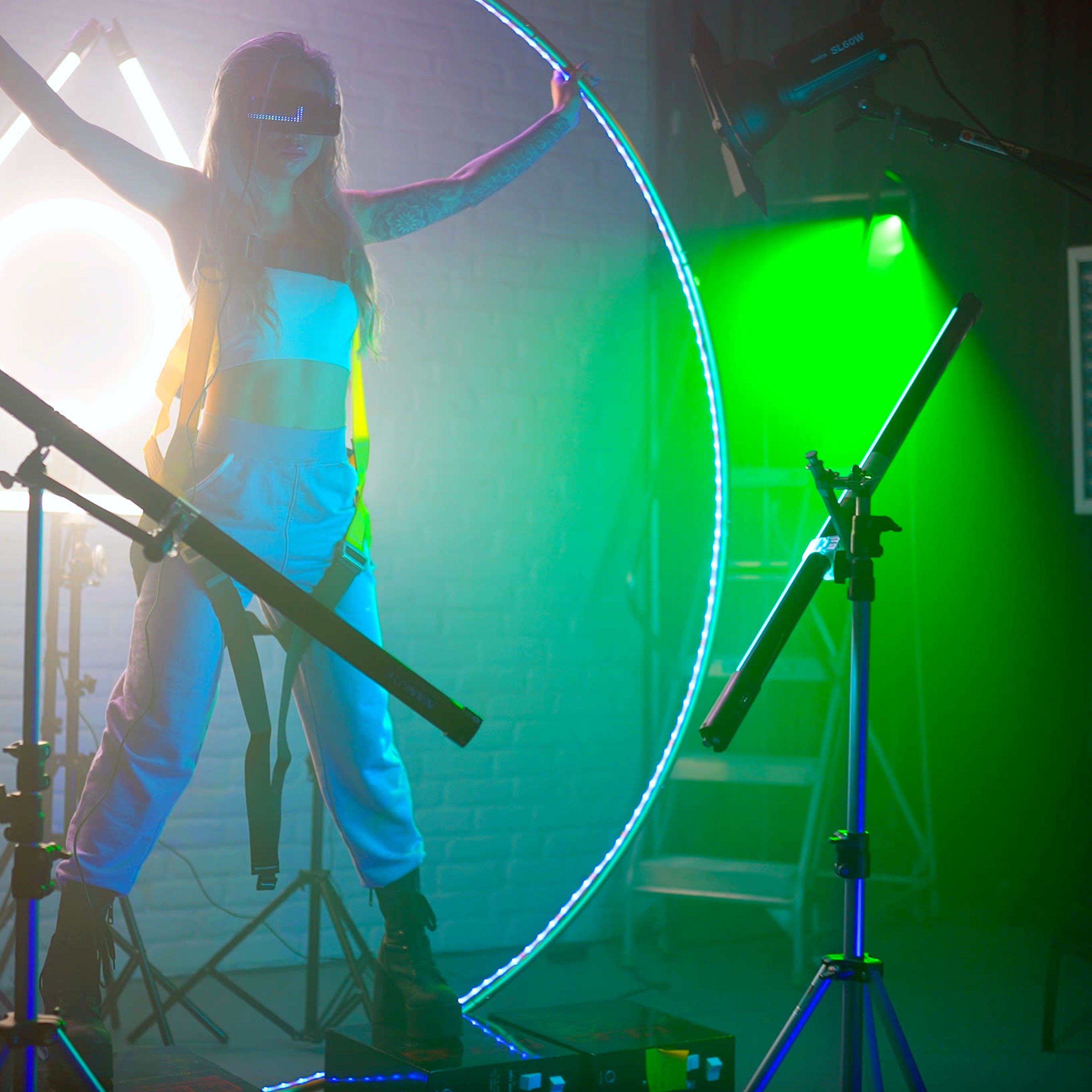 A figure stands in the center of a circular light setup surrounded by photography equipment and colorful lighting.