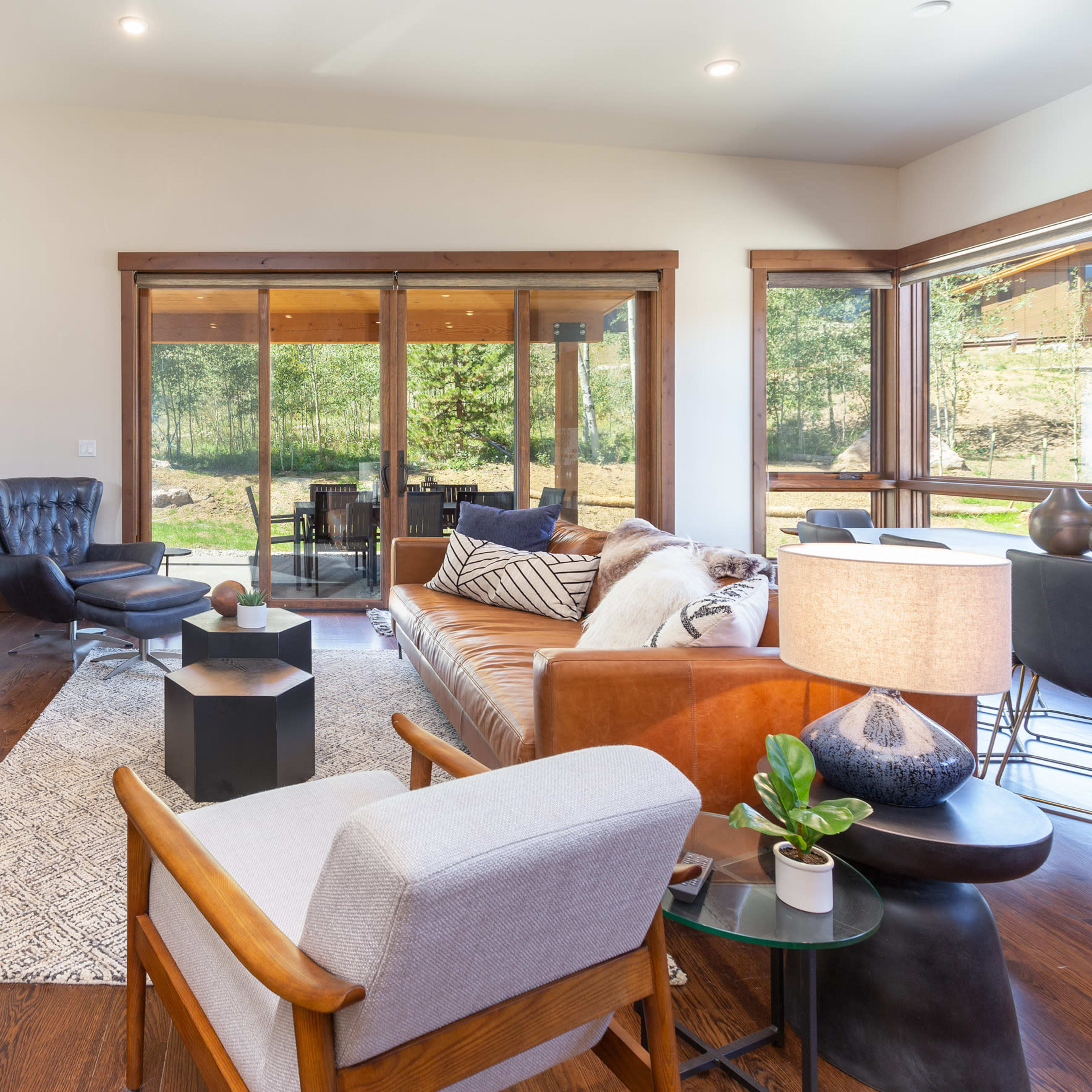 The living room features a stone fireplace, a leather sofa, and large windows that open to a view of the outdoor area.
