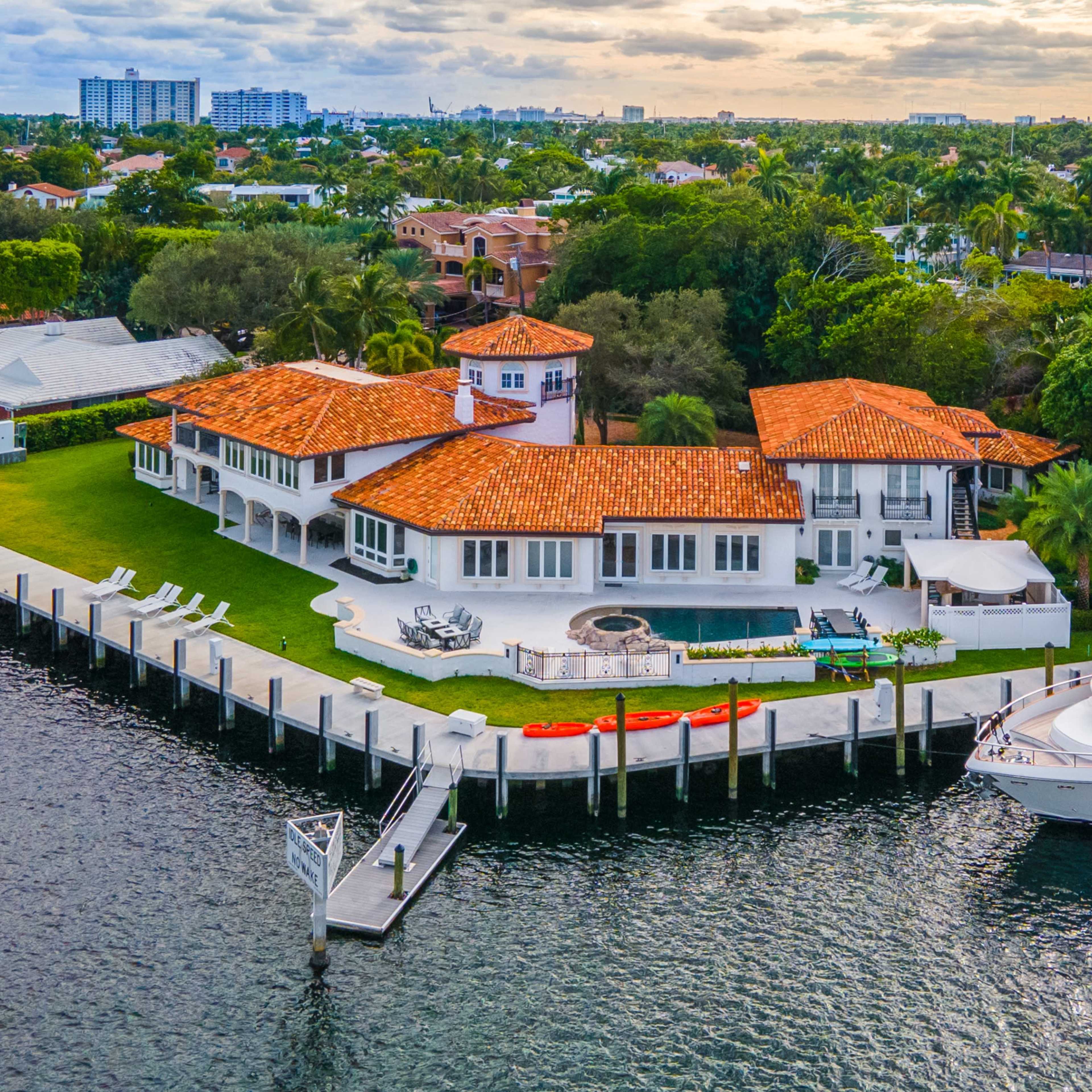 A waterfront luxury home with a large lawn, a swimming pool, and a docked yacht.