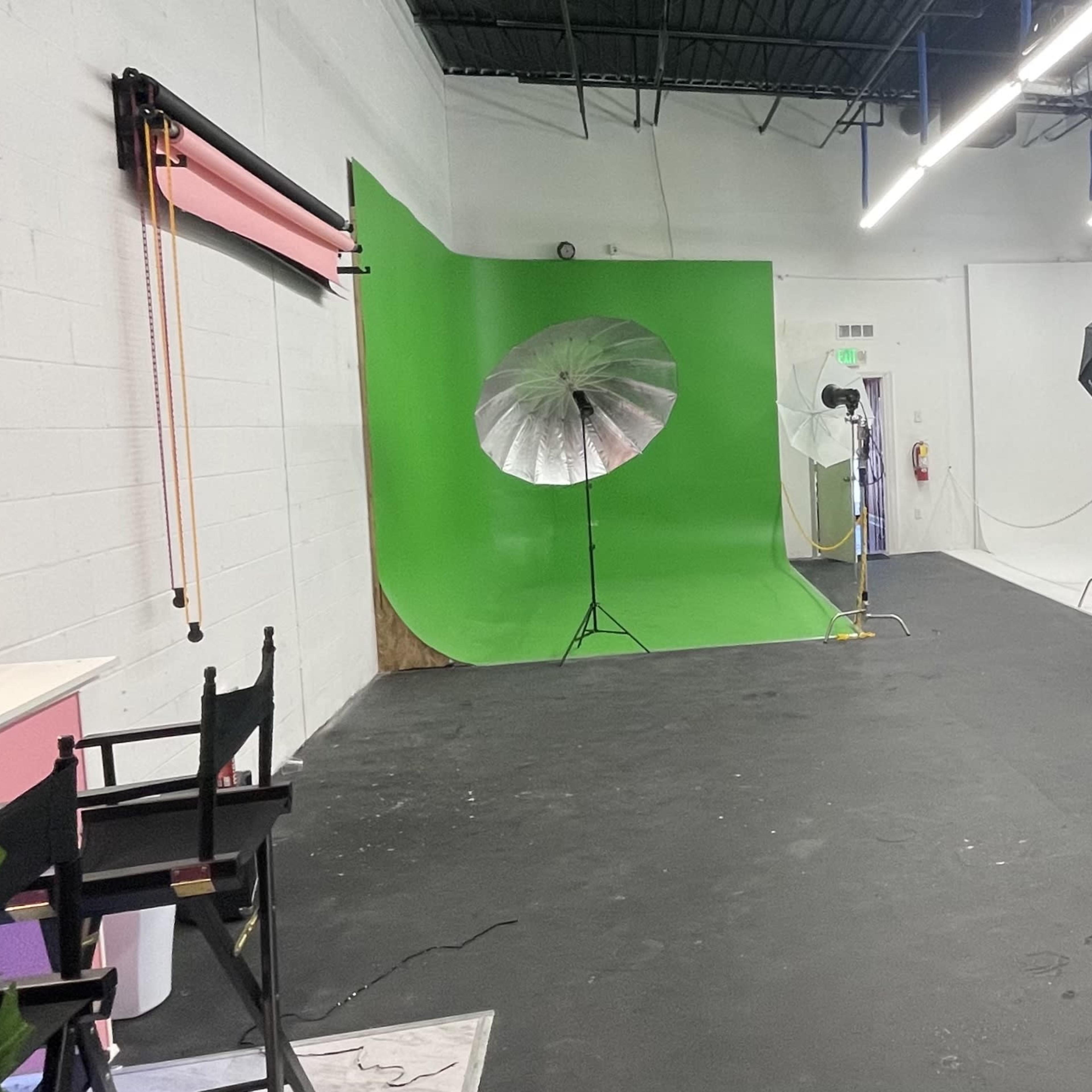 A photography studio with a green backdrop, various lighting equipment, and different backdrops on the walls.