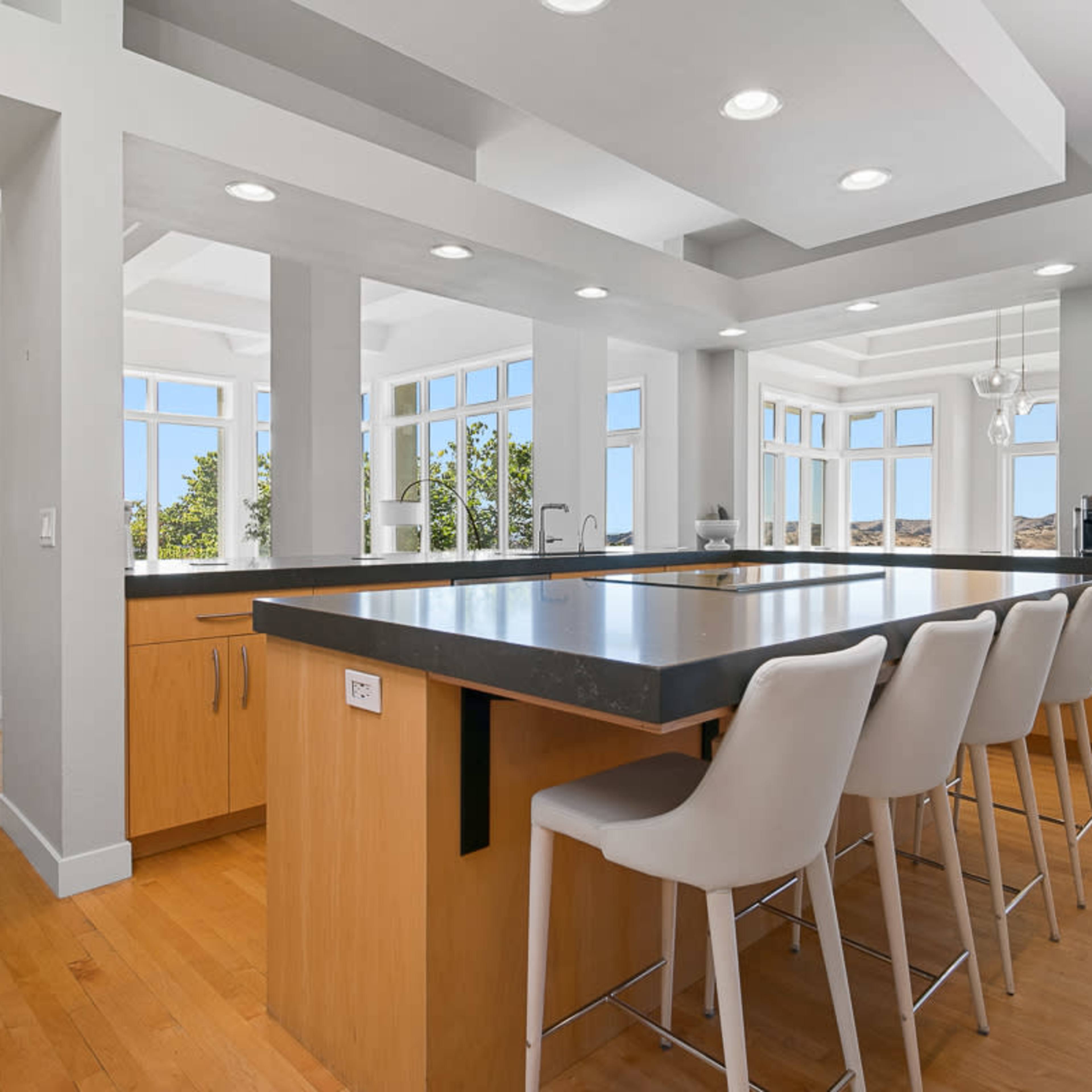 A modern kitchen with an island, surrounded by large windows that provide ample natural light.