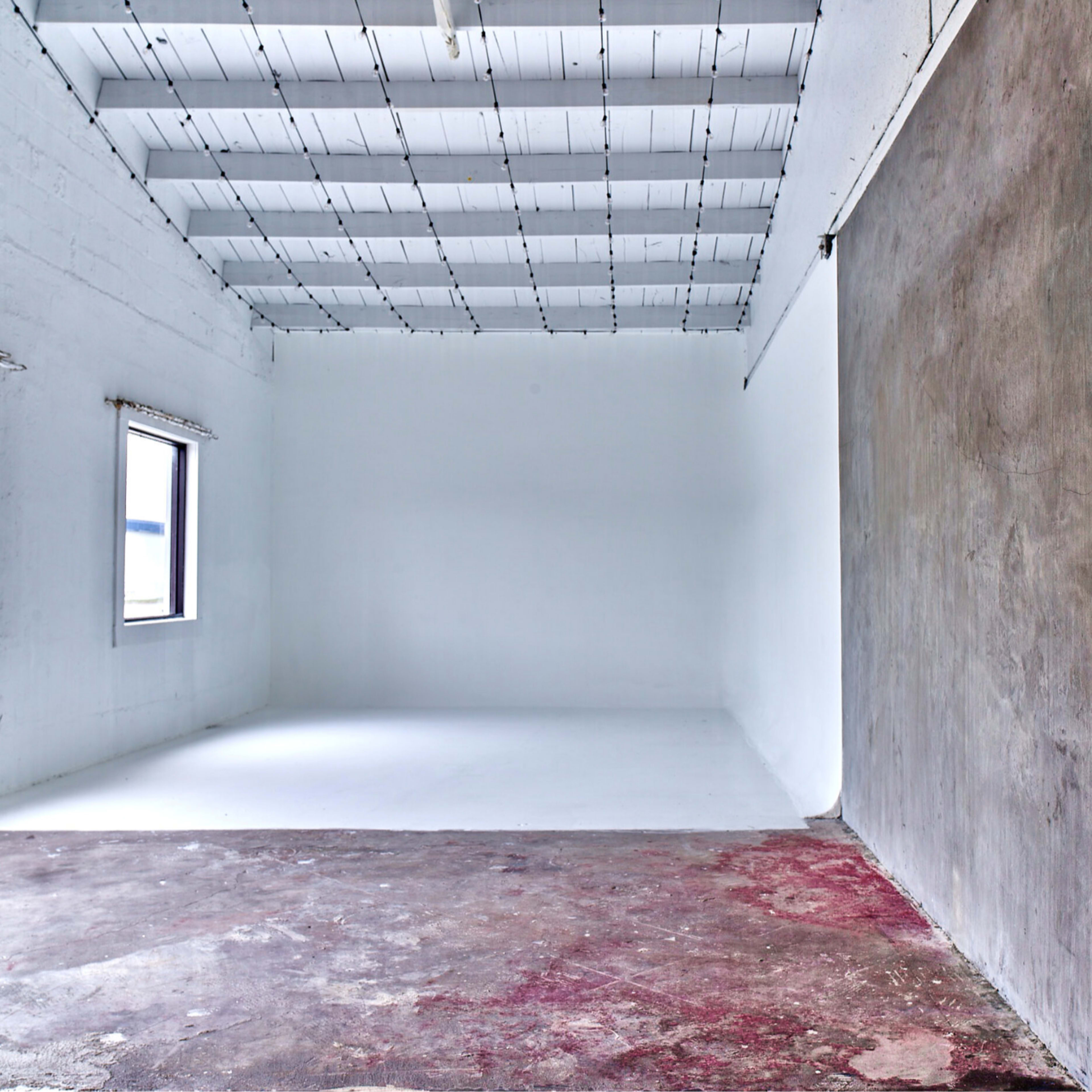 A spacious, empty room with a white ceiling, white walls, and a concrete wall on one side, featuring two windows.