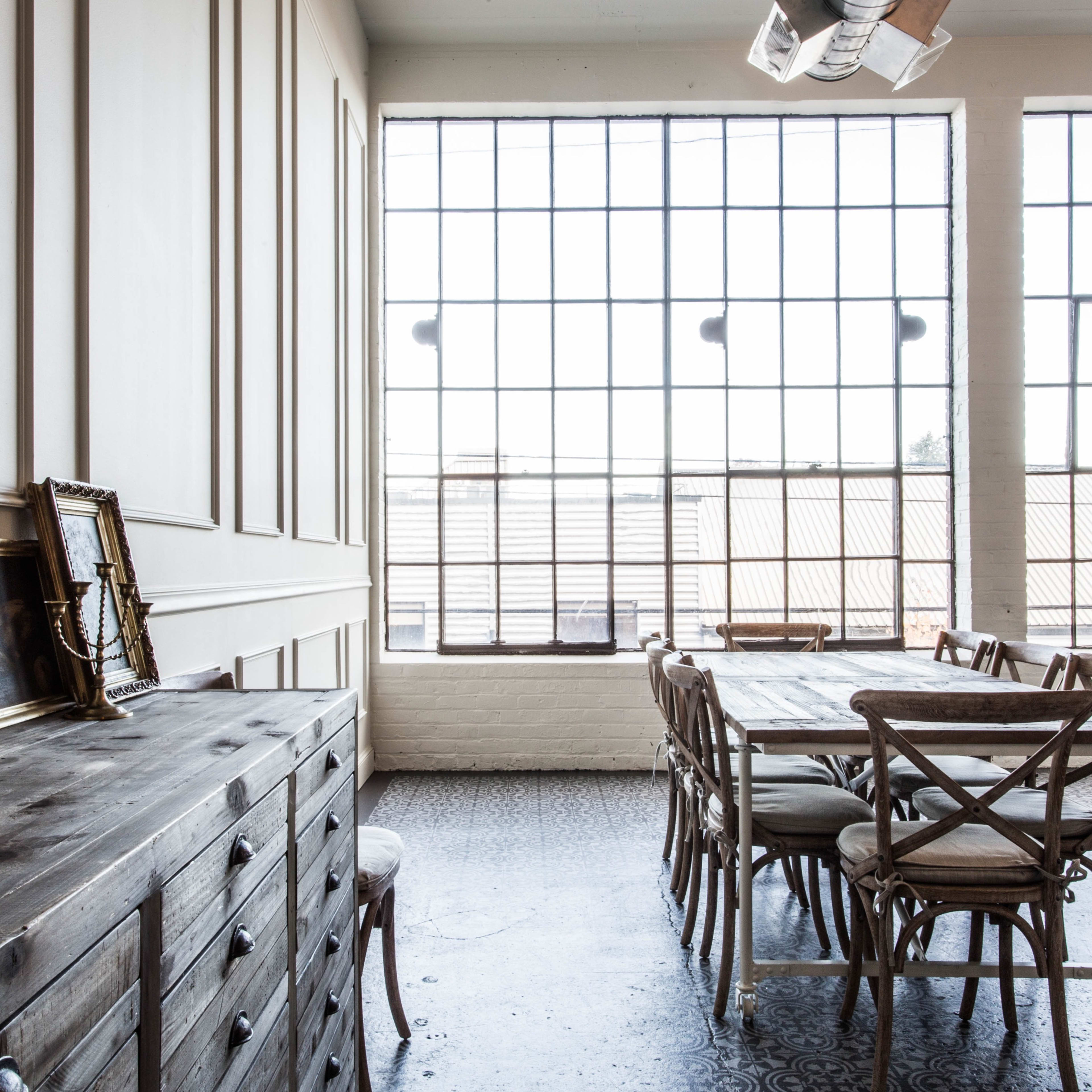 A spacious room with large windows, wooden furniture, and a long dining table accompanied by chairs.
