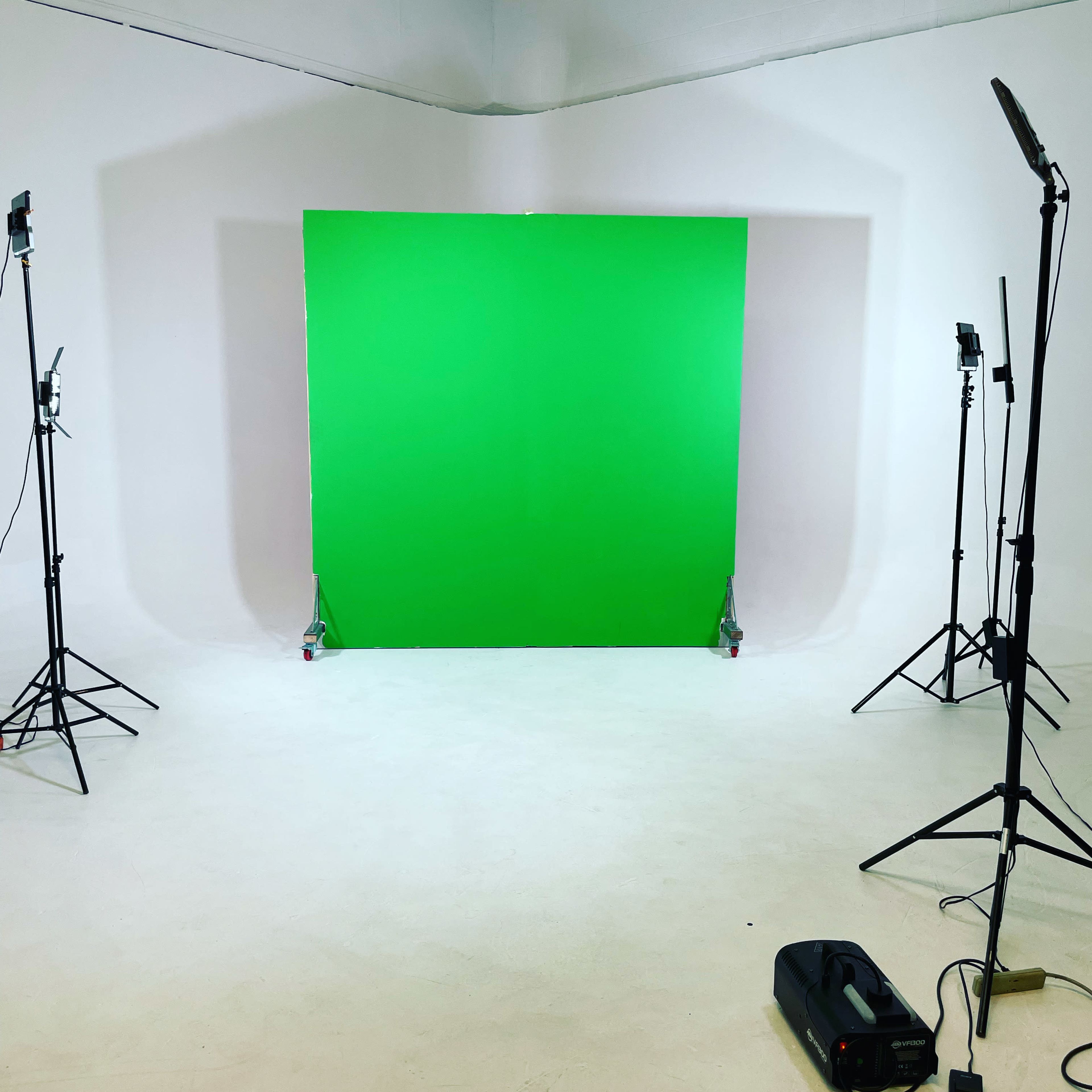 A photography studio with a green screen set up in the center, surrounded by lighting equipment on stands.