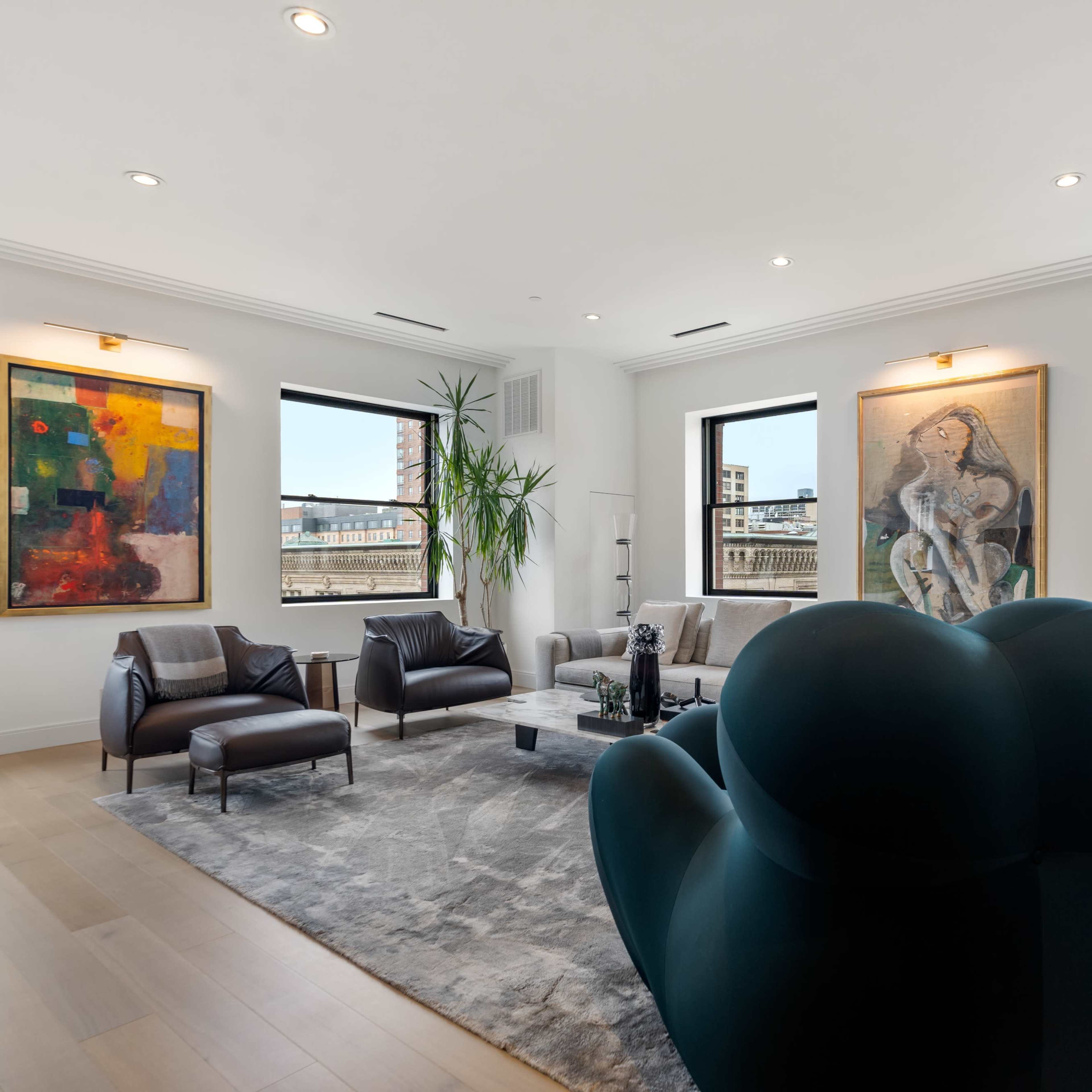 The room features modern furniture, large windows with urban views, and two abstract paintings on the walls.