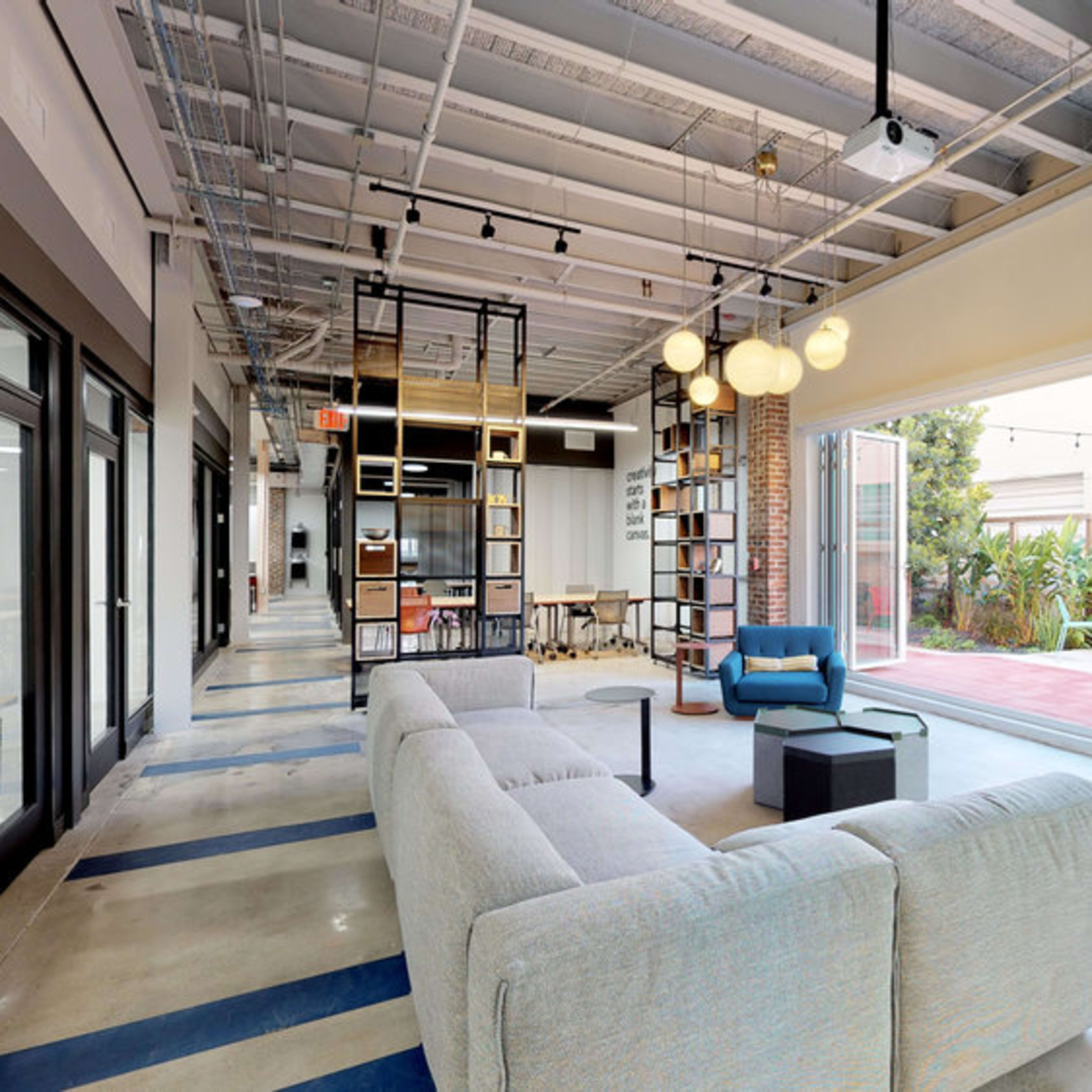 A modern office space featuring a gray sofa, a bookshelf, and large glass doors that open to an outdoor area with seating.
