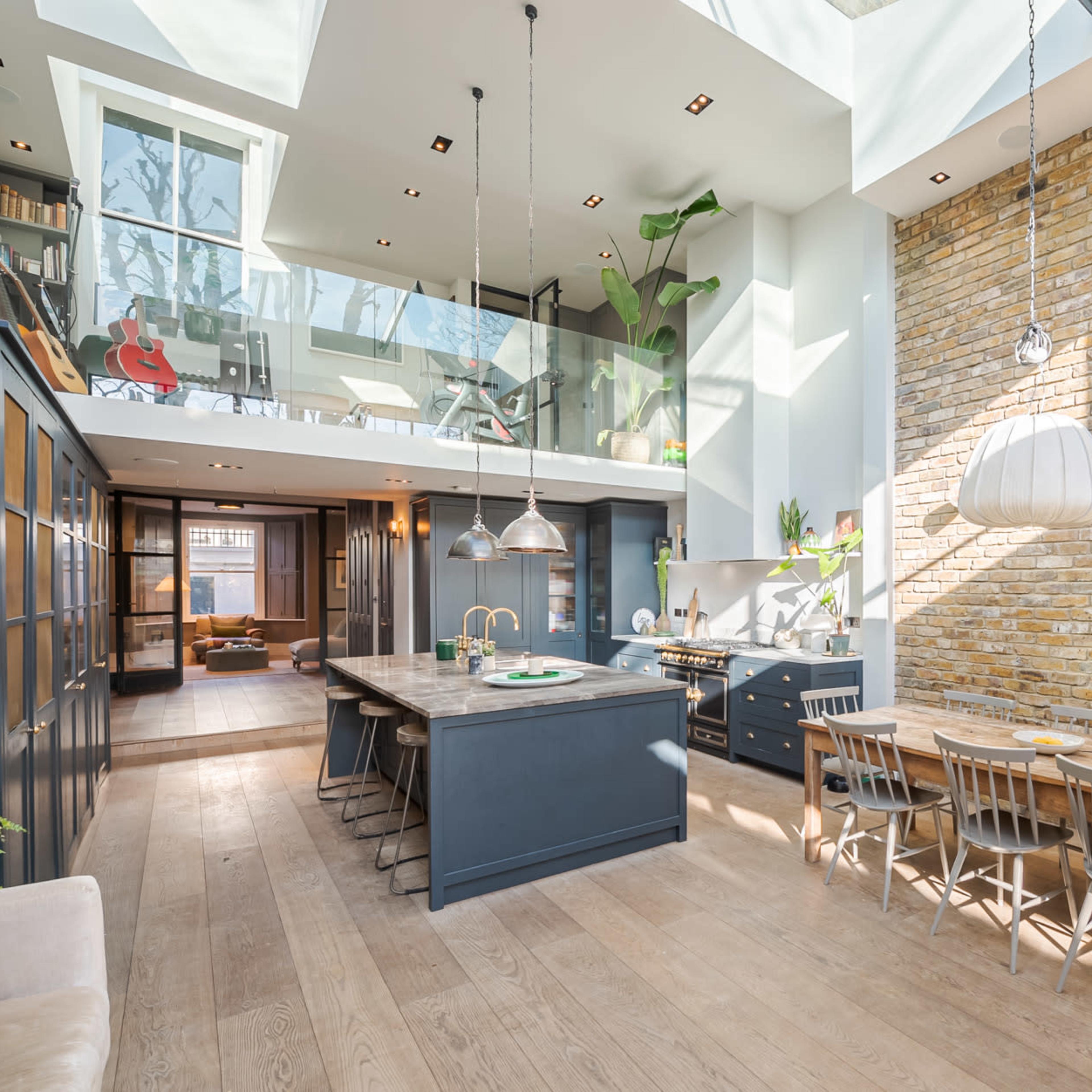 A modern kitchen and dining area with exposed brick walls, a large island, and ample natural light streaming through a skylight.