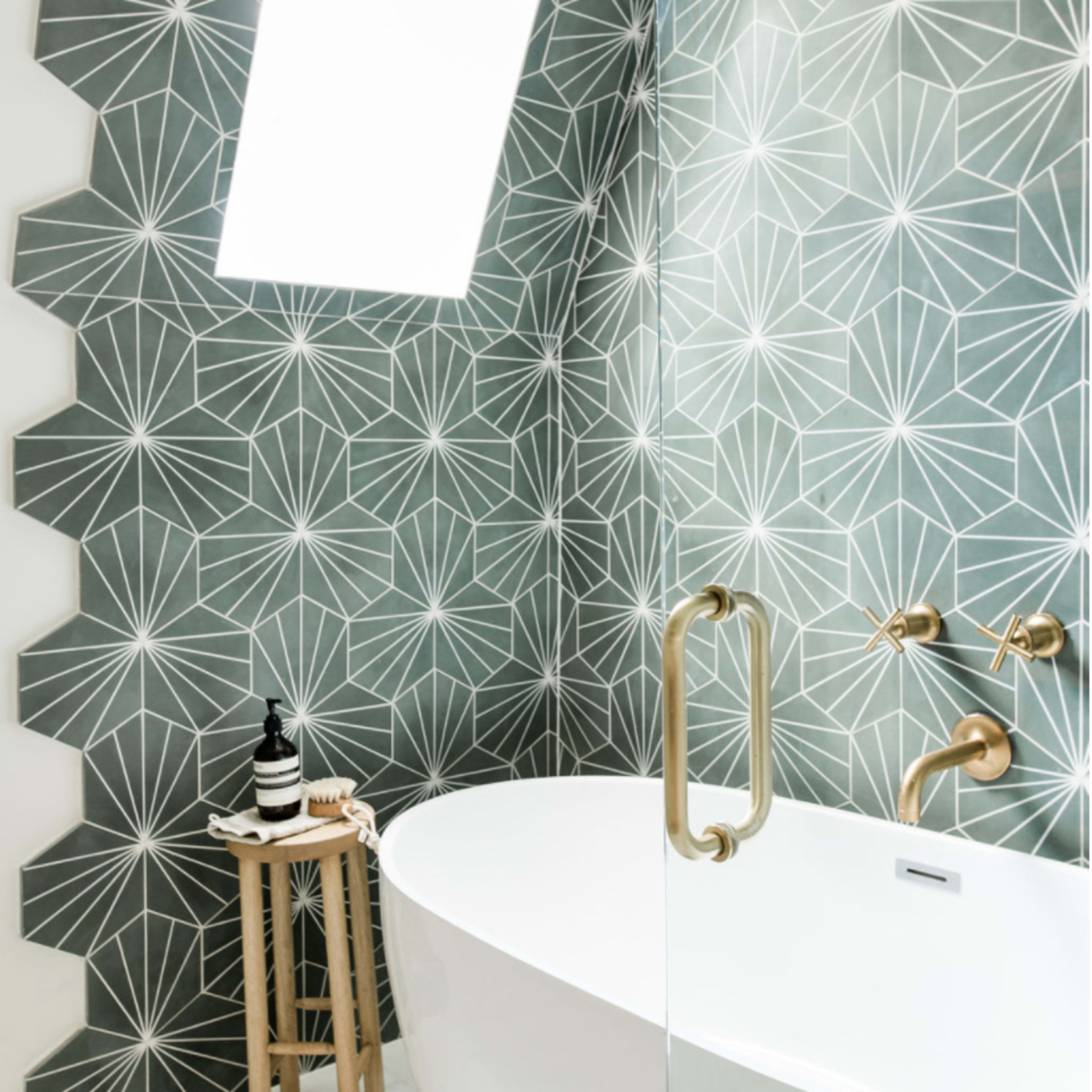 The bathroom features a freestanding white tub alongside a green geometric tile wall and a skylight.