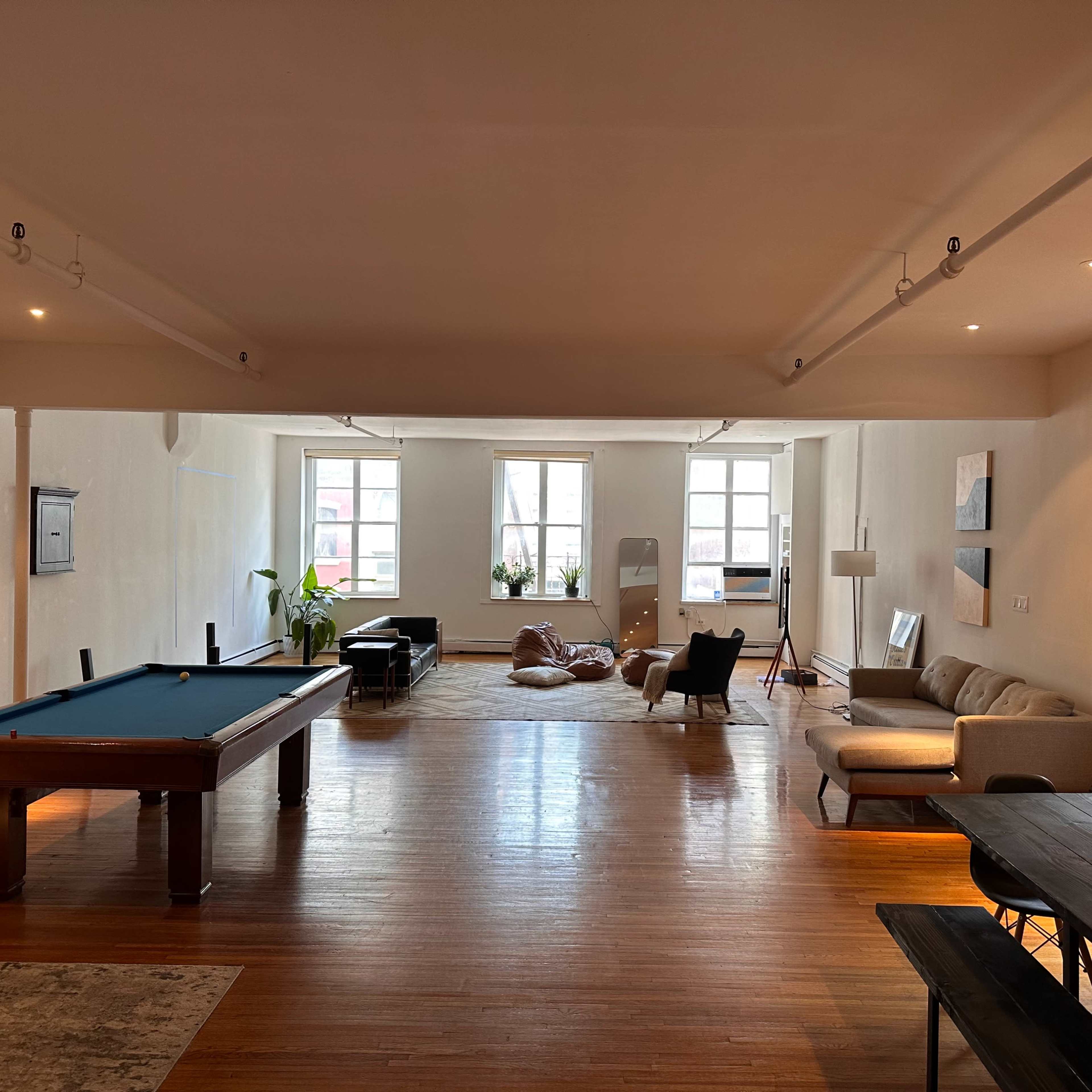 A spacious, open living area featuring a pool table, lounge seating, and large windows that illuminate the wooden floor.