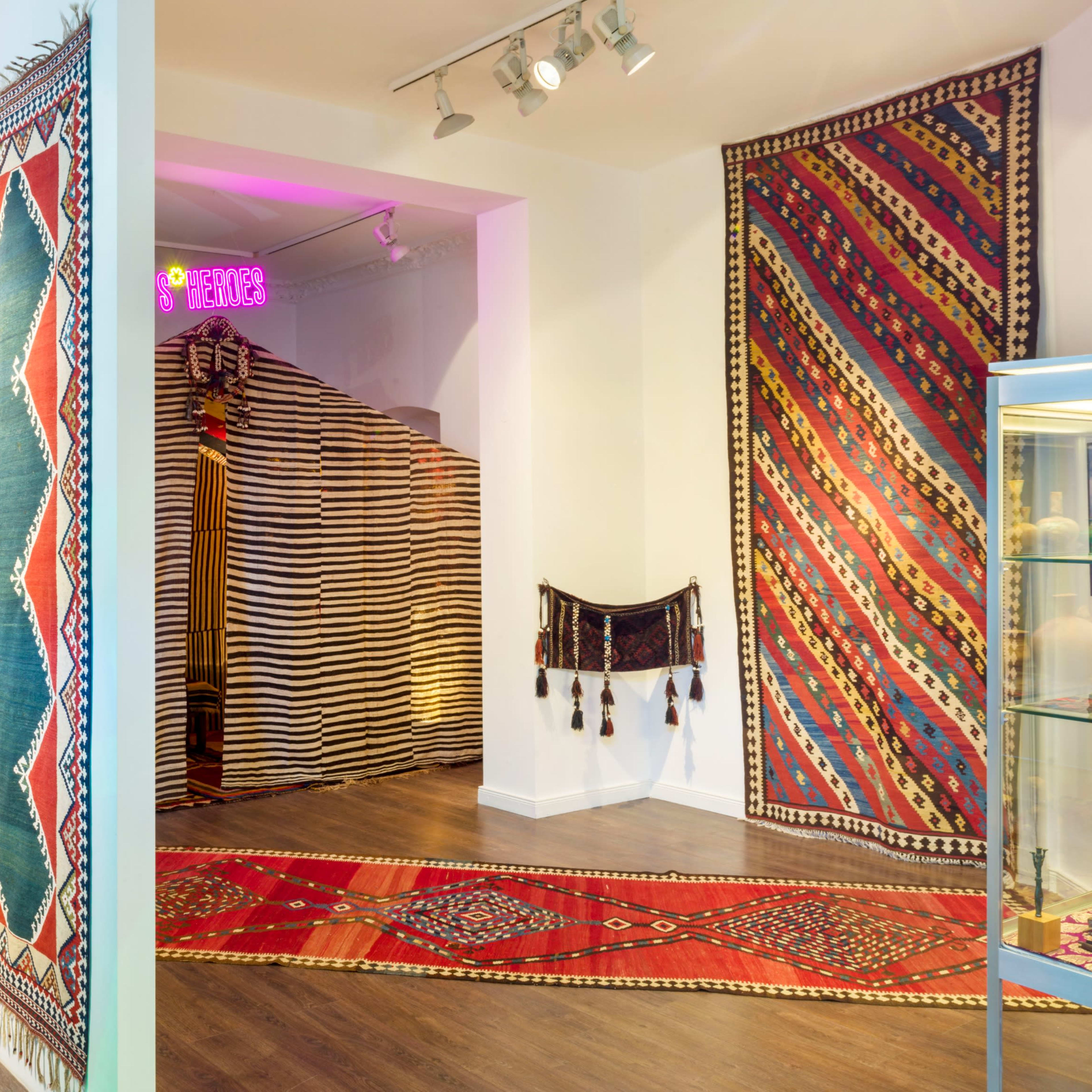 A gallery space featuring colorful textile artworks displayed on the walls and a glass case containing decorative items.