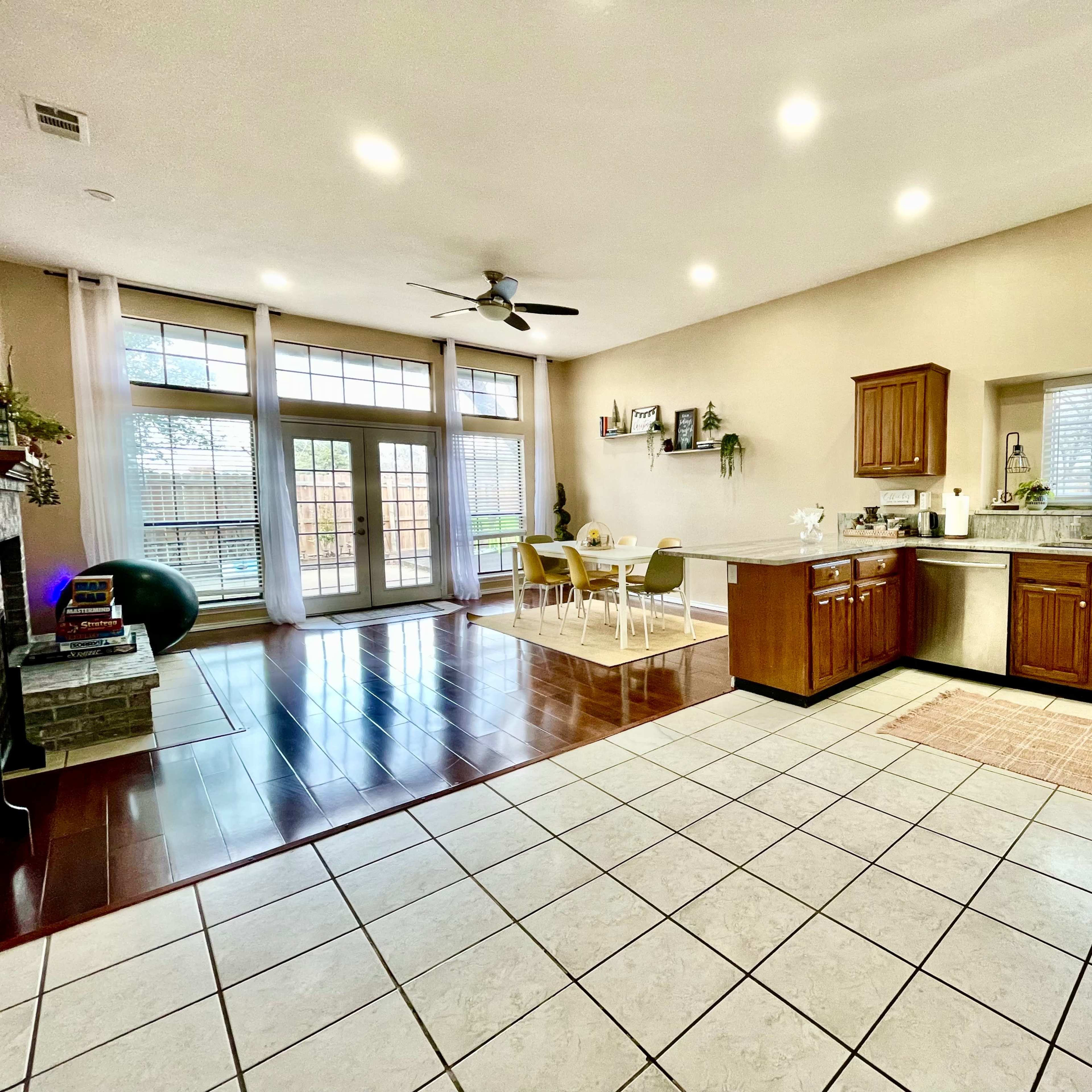 A spacious kitchen and dining area with wooden cabinetry, a tiled floor, and large windows allowing natural light to enter.