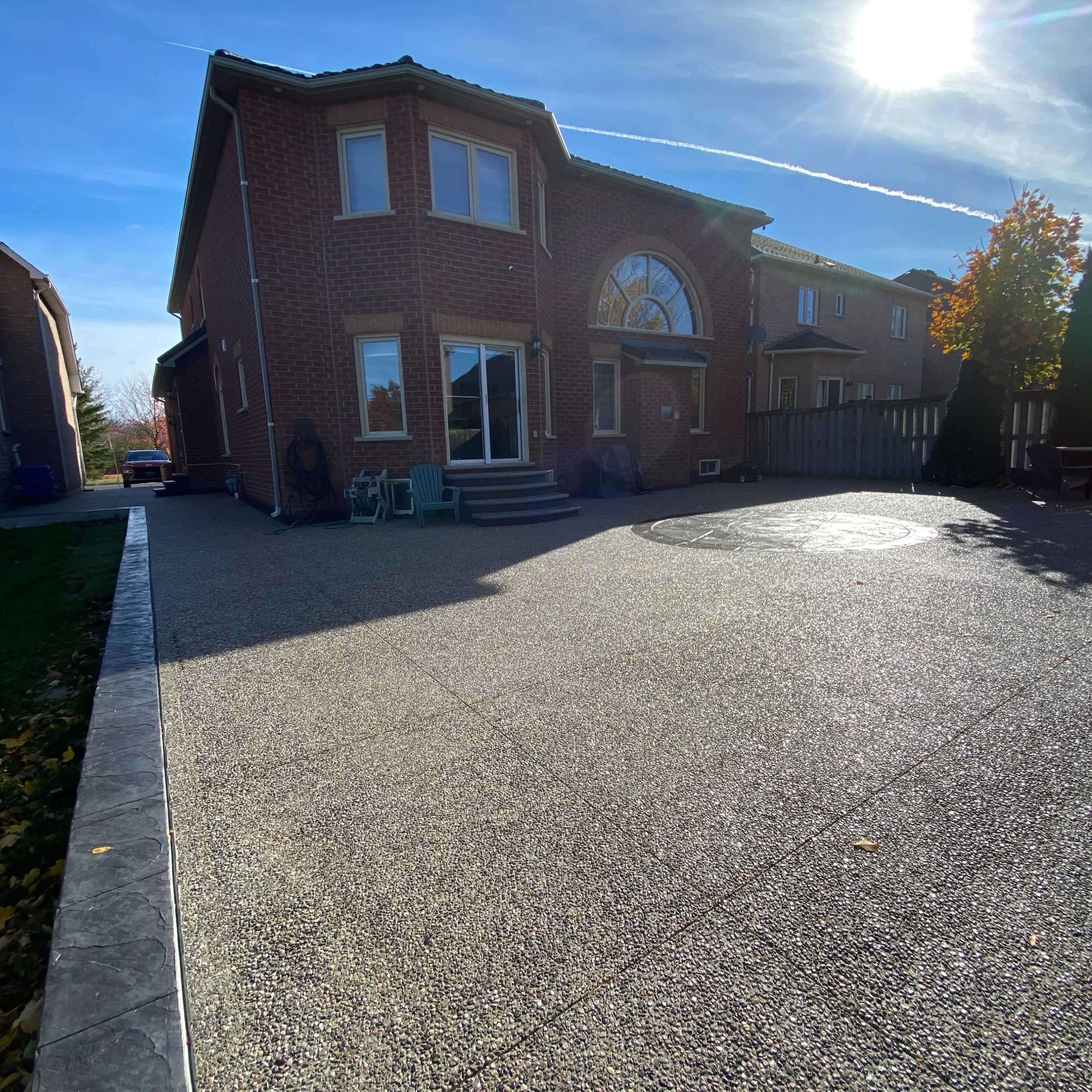 A brick house features a large driveway with a circular design, under a clear blue sky with the sun shining brightly.