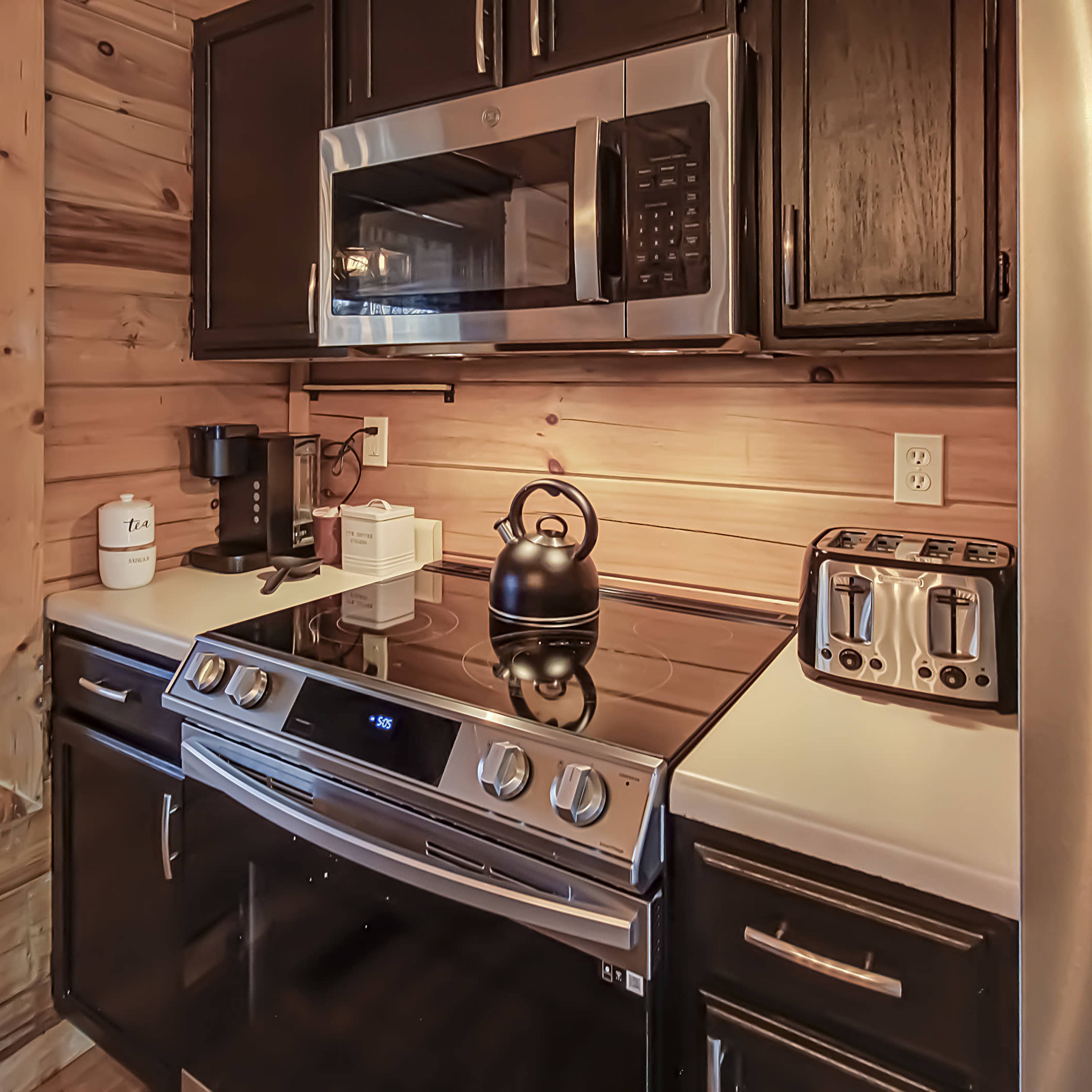 A kitchen with wooden walls, featuring stainless steel appliances, including a microwave, stove, and toaster, along with a coffee maker and kettle.