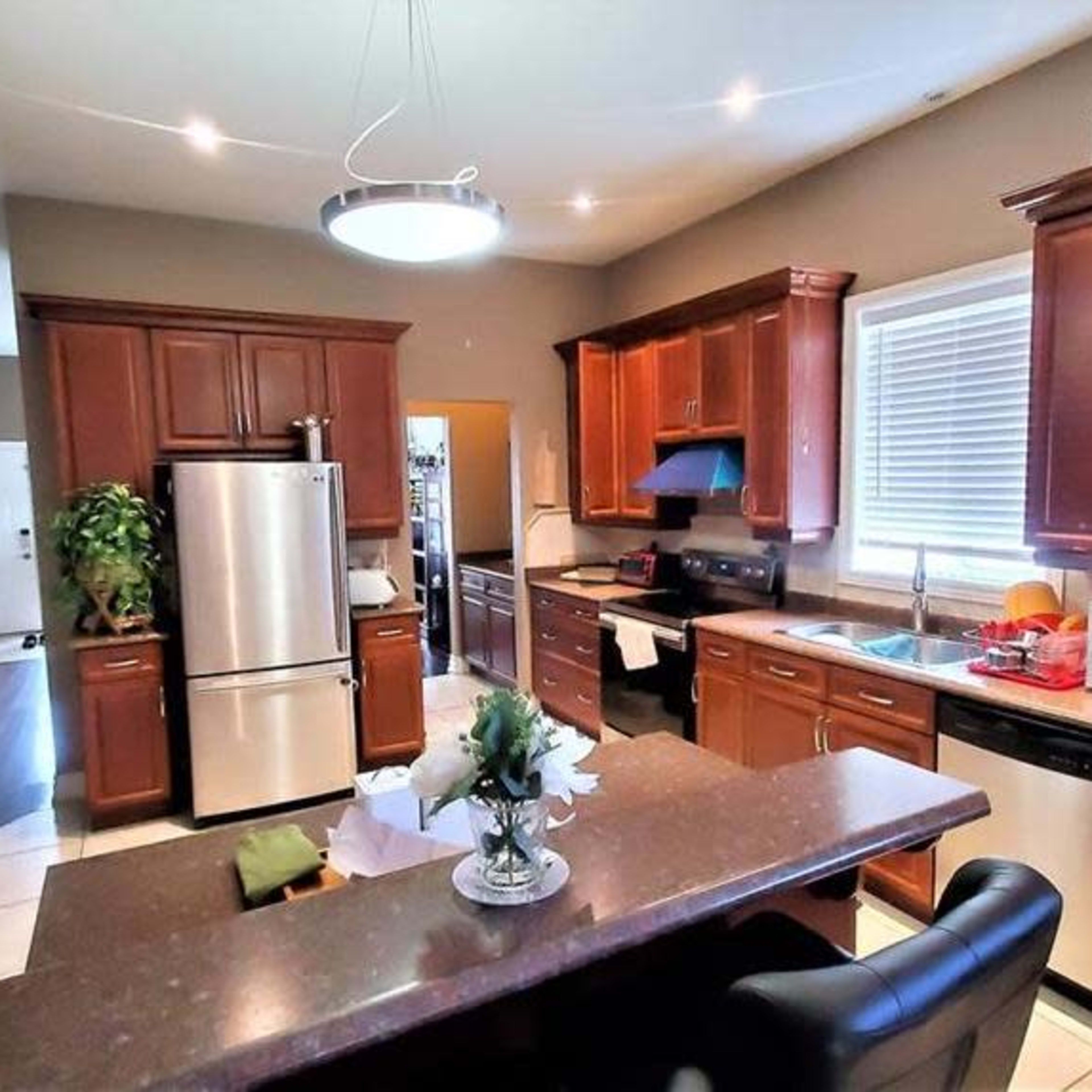A modern kitchen with wooden cabinetry, stainless steel appliances, a central island, and a window with light streaming in.