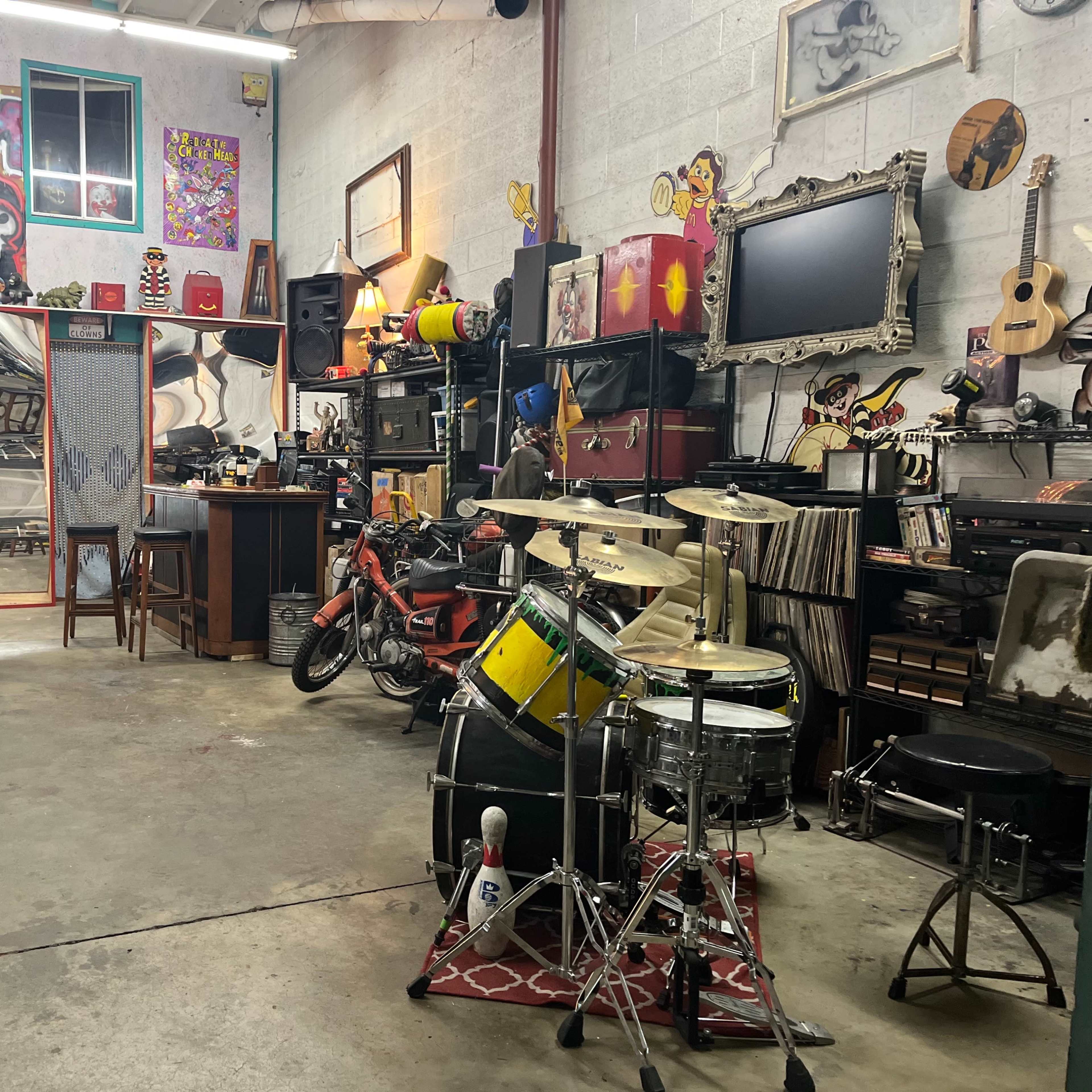 A cluttered workshop or garage space filled with musical instruments, artwork, and various tools.