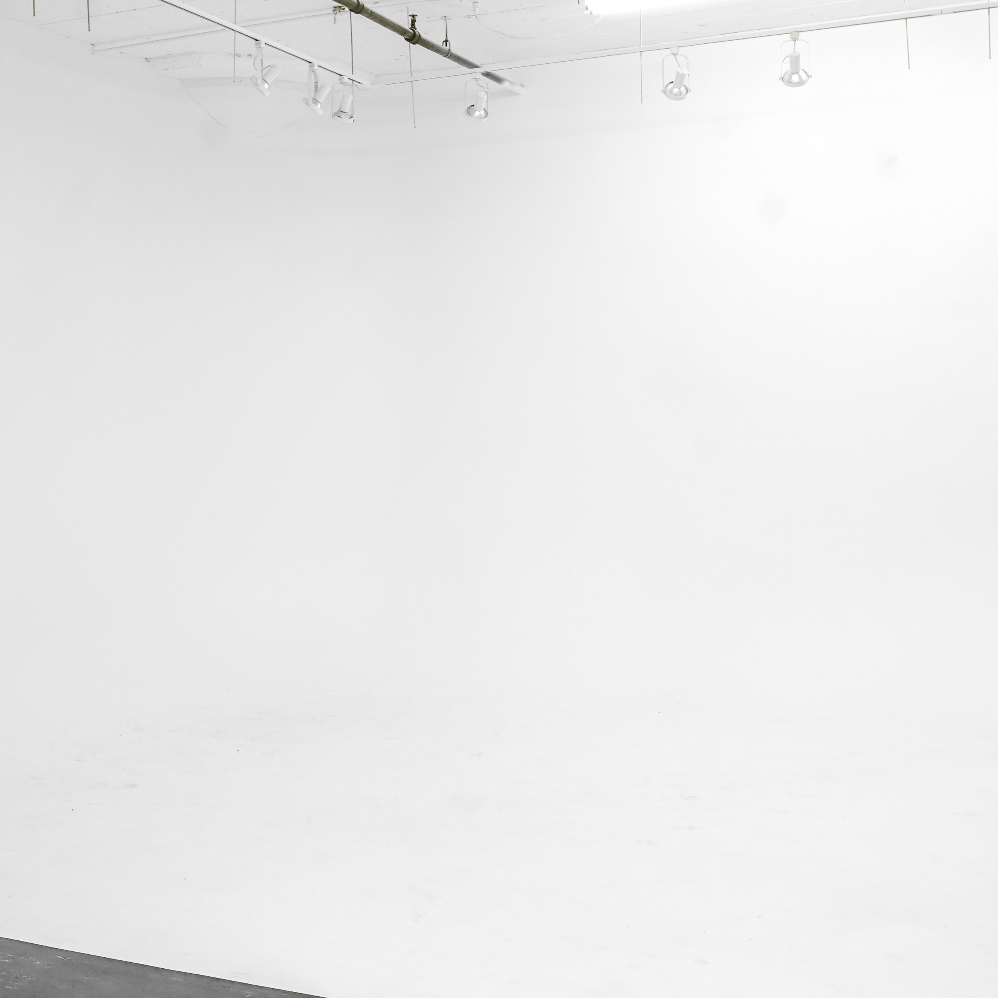 A spacious, empty studio with a white backdrop and polished floor.