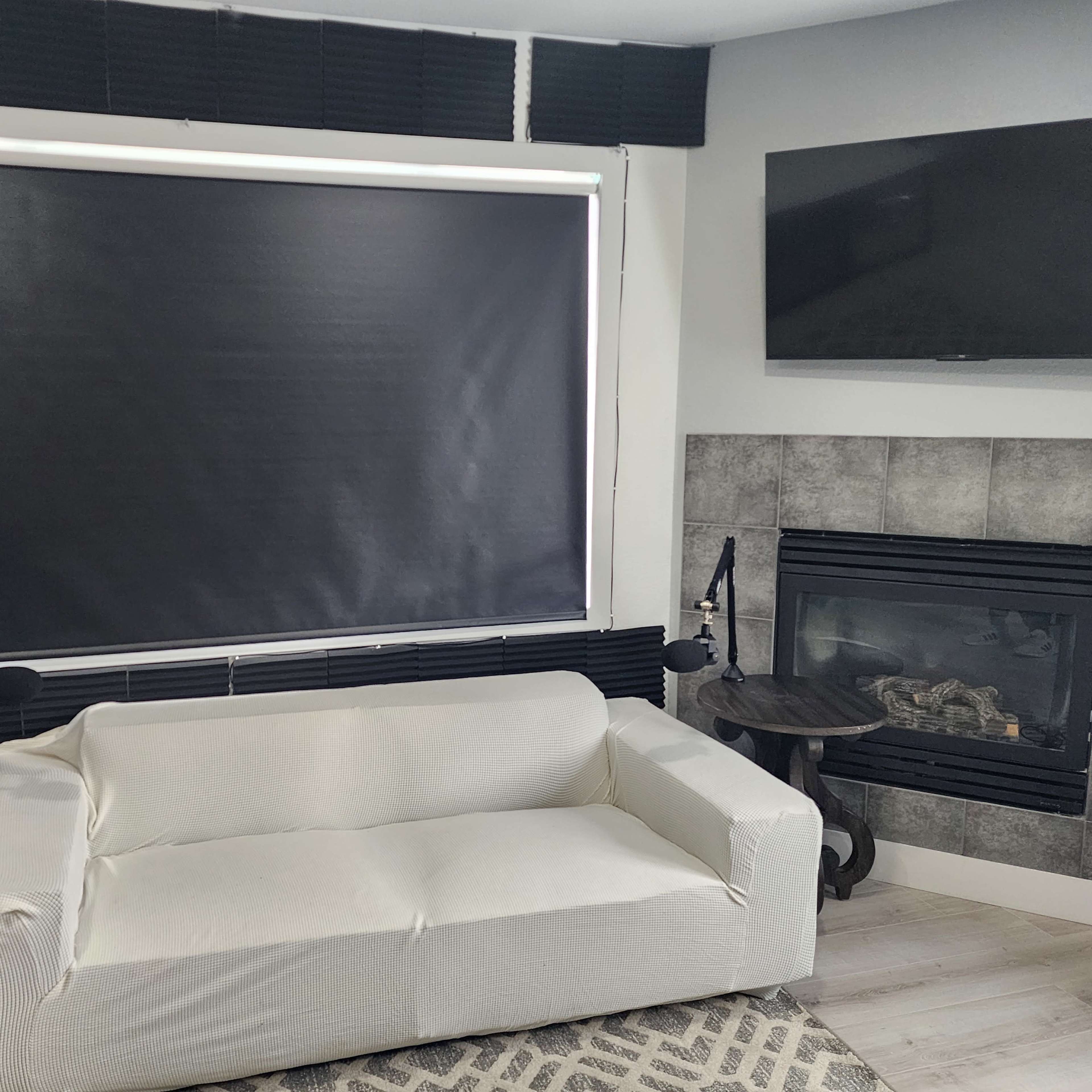 A living room with a white couch, dark window coverings, two side tables, and a fireplace against a tiled wall.