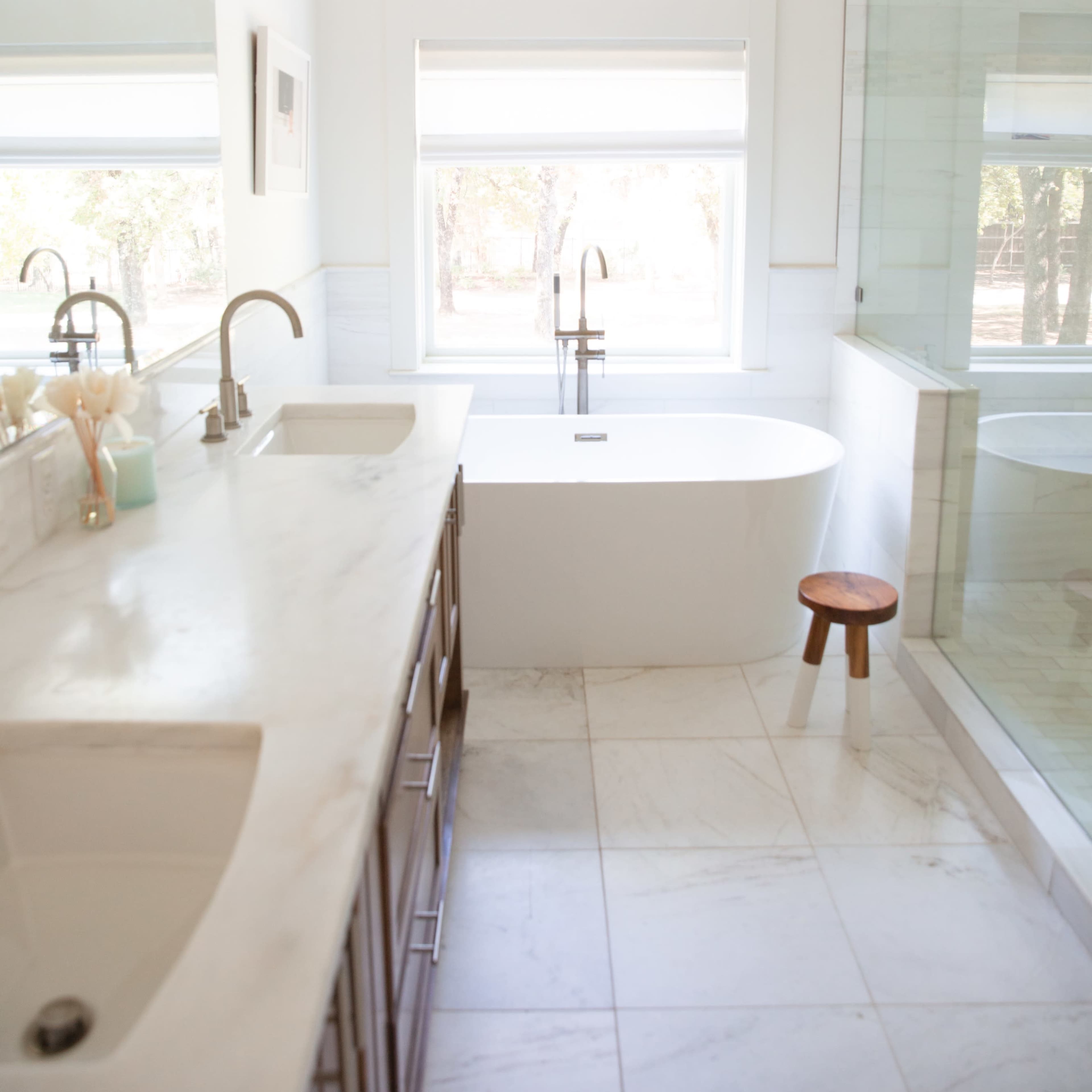 A spacious, modern bathroom featuring a freestanding bathtub, double sinks, and a glass shower enclosure with natural light streaming in through large windows.