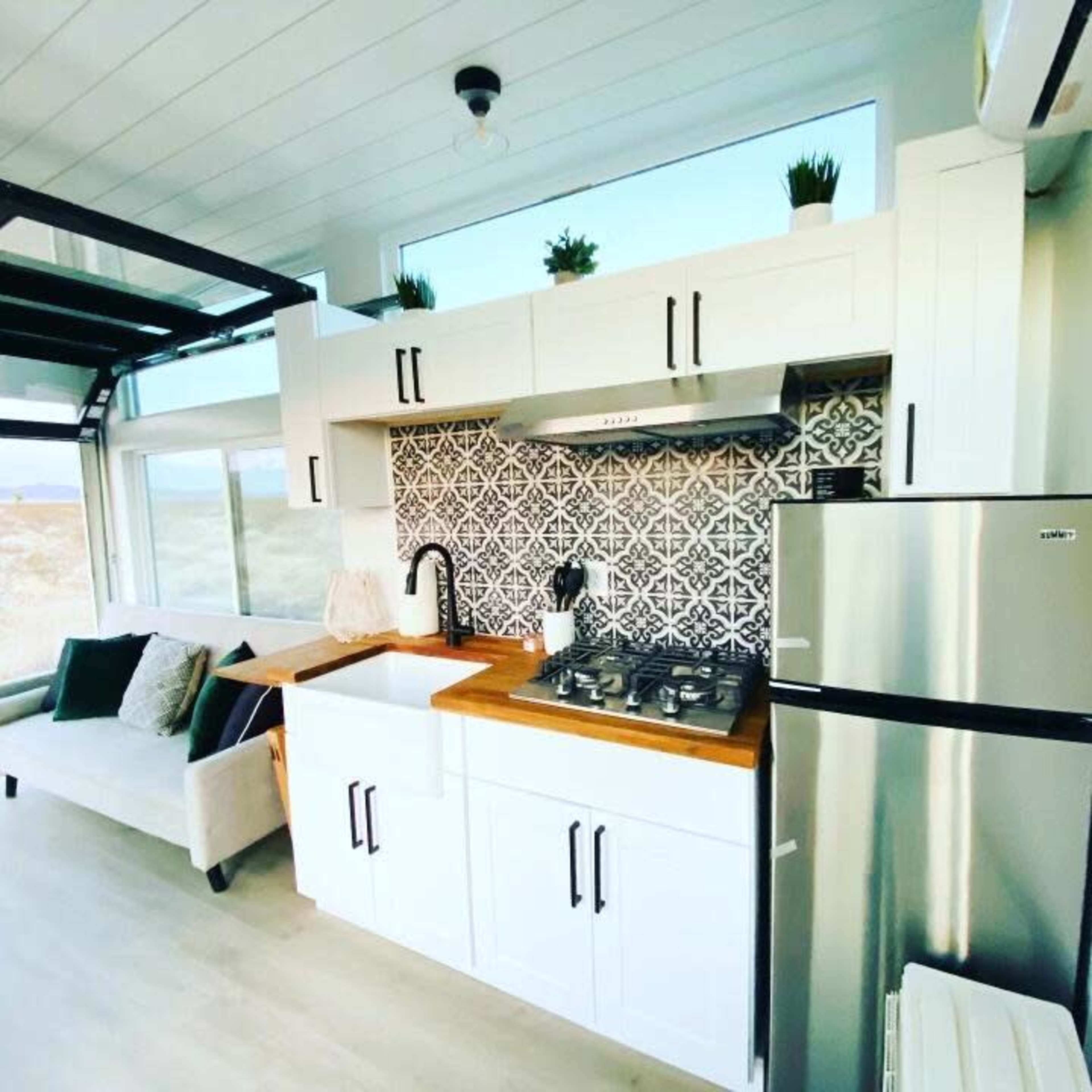 A modern kitchen with white cabinets, a farmhouse sink, a stainless steel refrigerator, and a patterned backsplash.