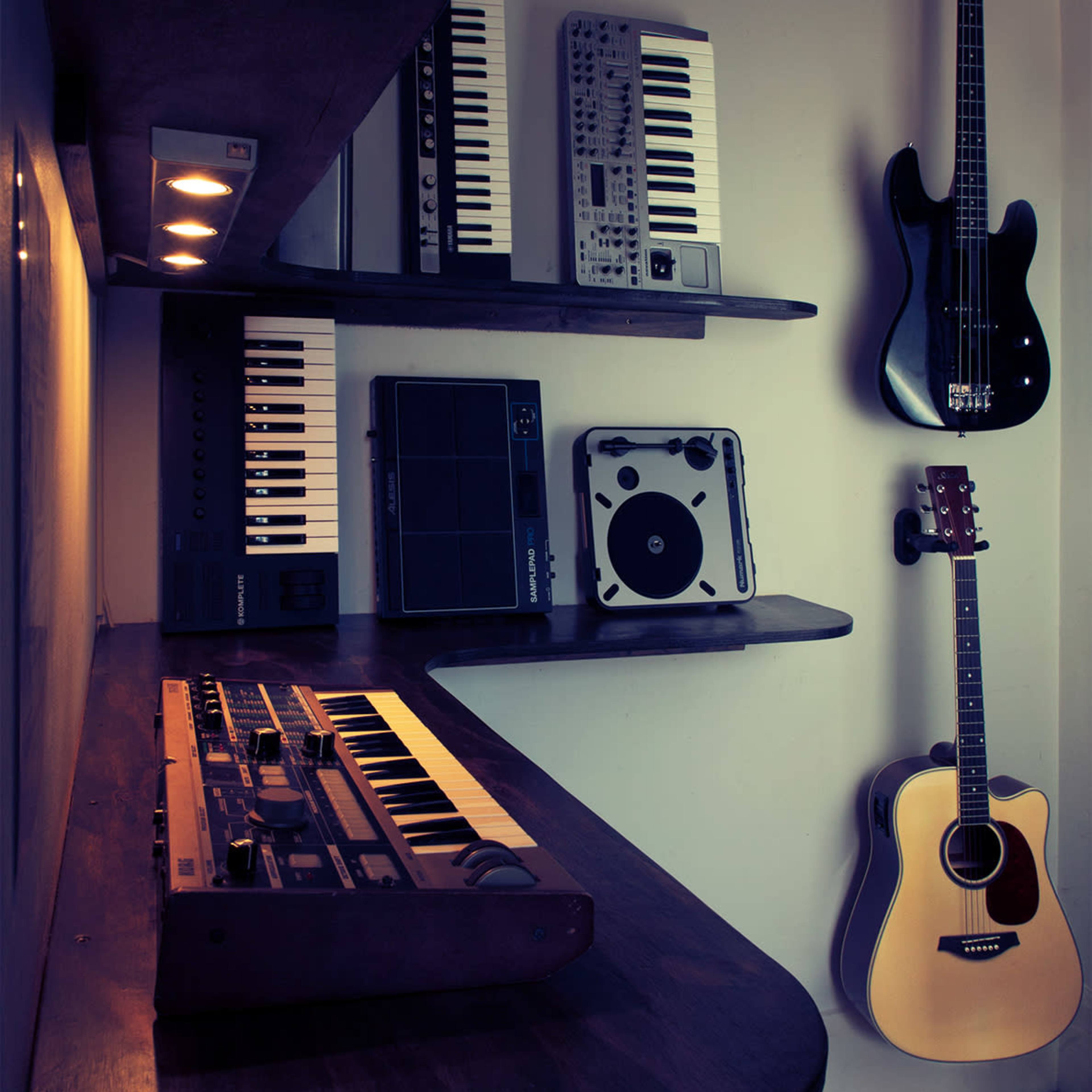 A collection of musical instruments and equipment displayed on shelves, including keyboards, a drum pad, and an acoustic guitar, mounted on a wall.