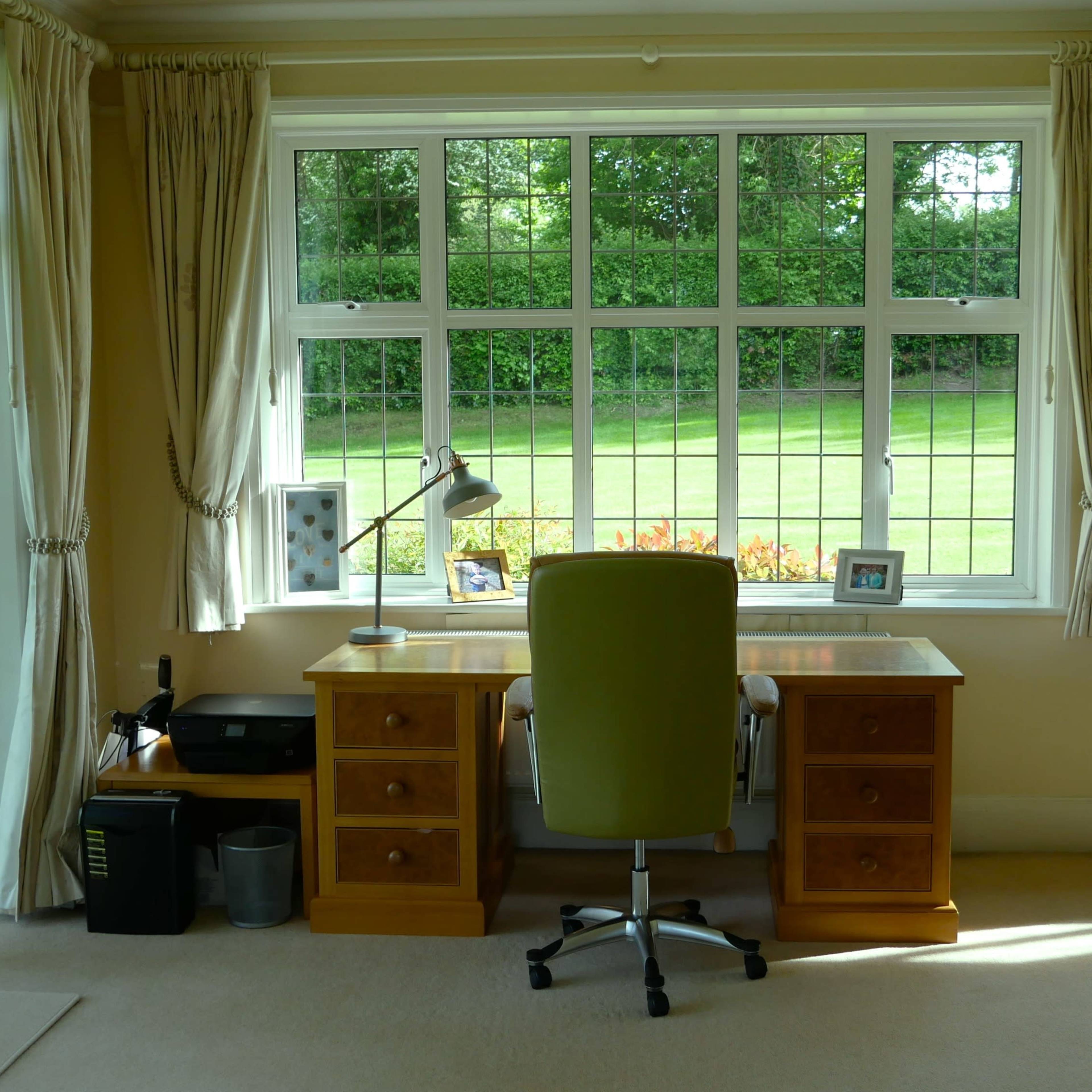 A well-lit office space with a wooden desk and green chair positioned next to large windows overlooking a grassy area.
