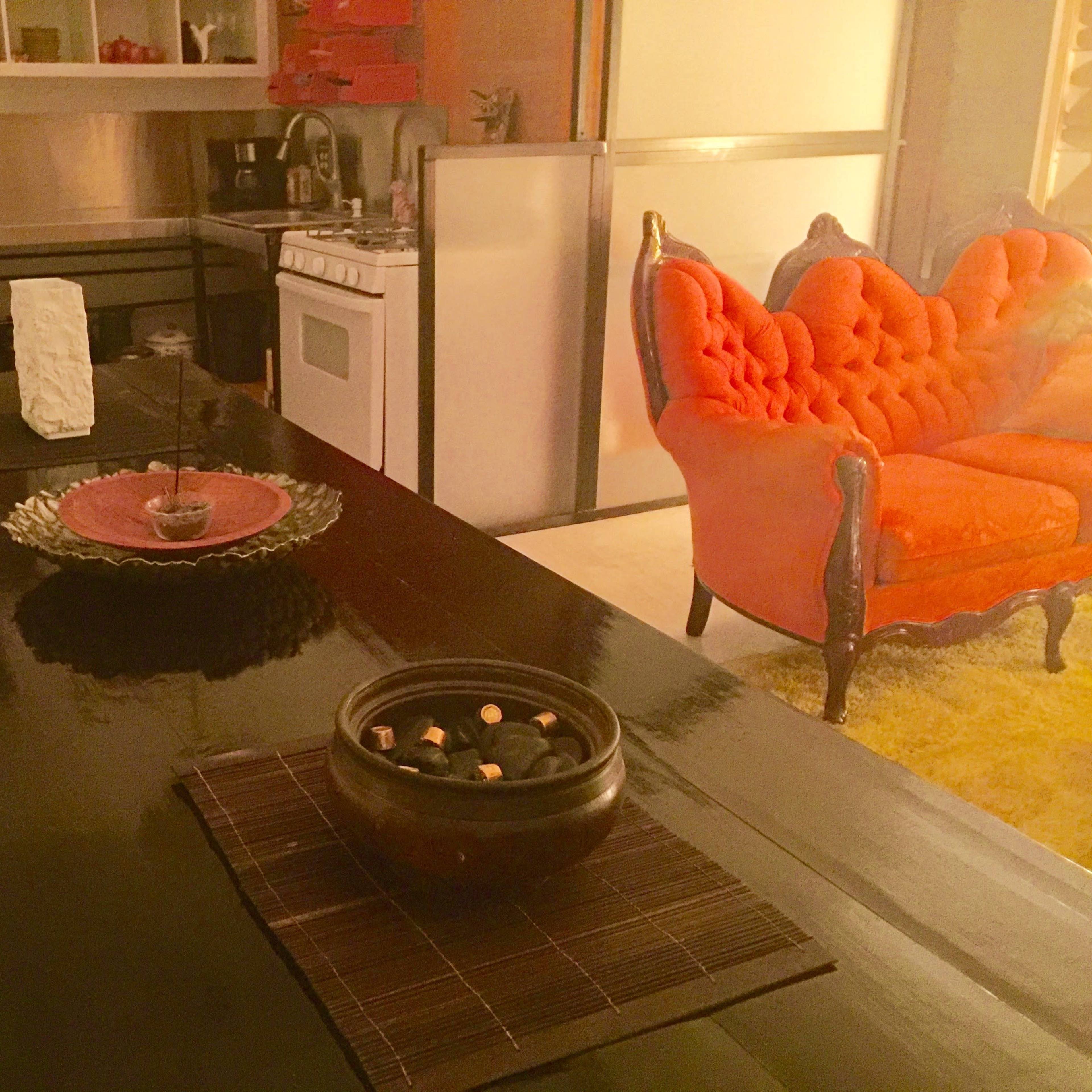 A modern kitchen and living area featuring an orange tufted sofa, a black dining table, and decorative items on the table.