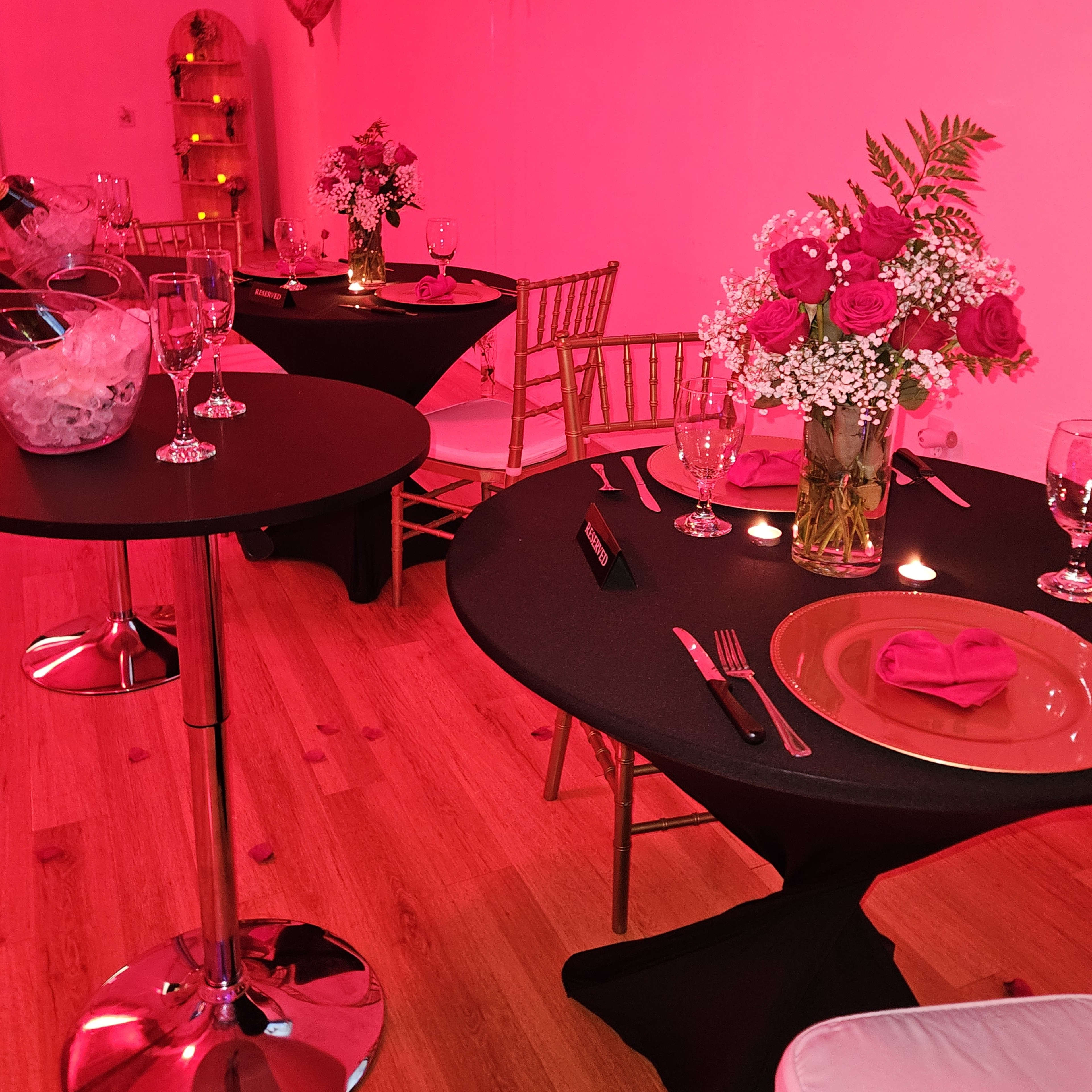 The scene features elegantly set tables with black tablecloths, floral arrangements, and pink lighting in a decorated event space.