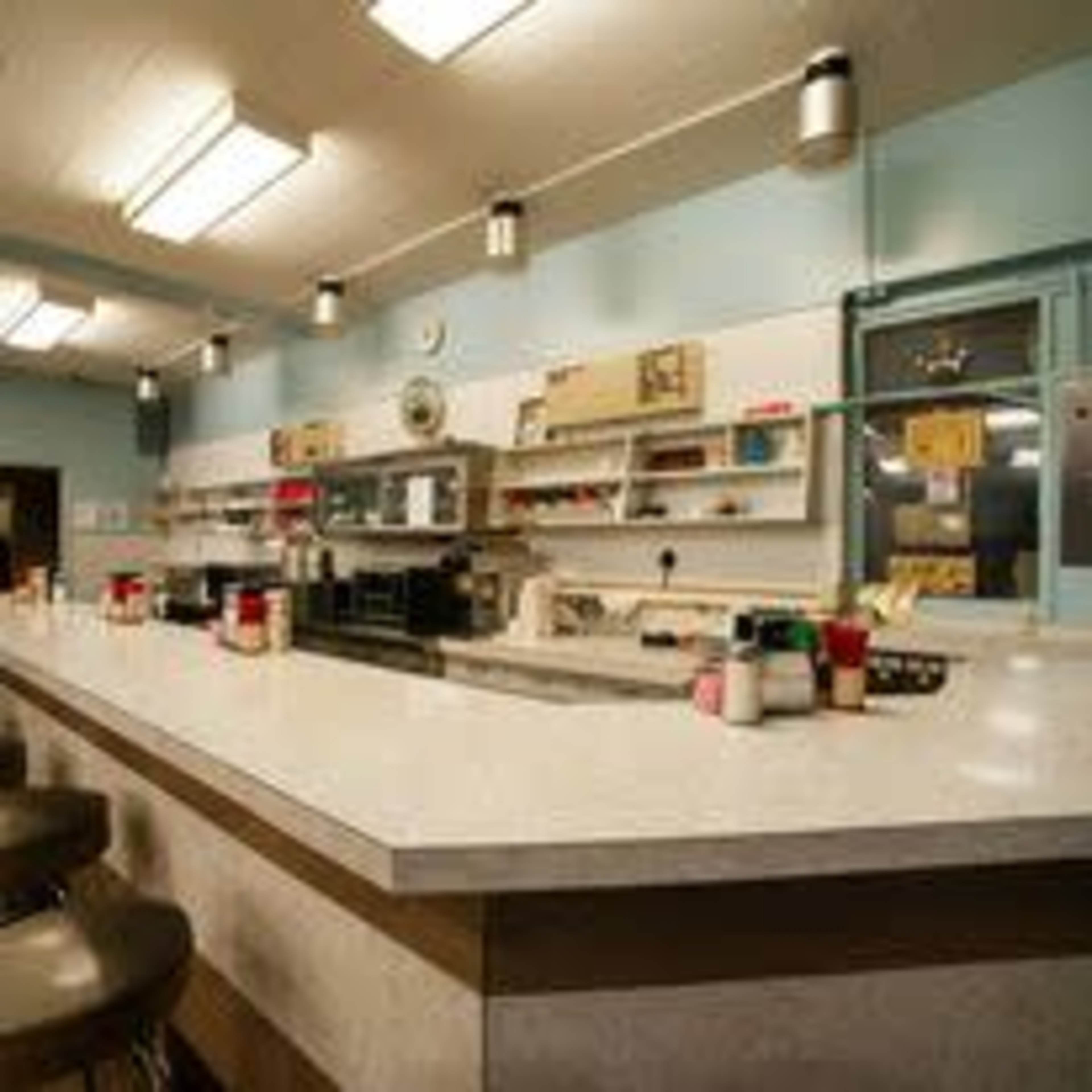 A retro diner counter with bar stools, a long marble surface, and shelves displaying various condiments and kitchen items against a blue wall.
