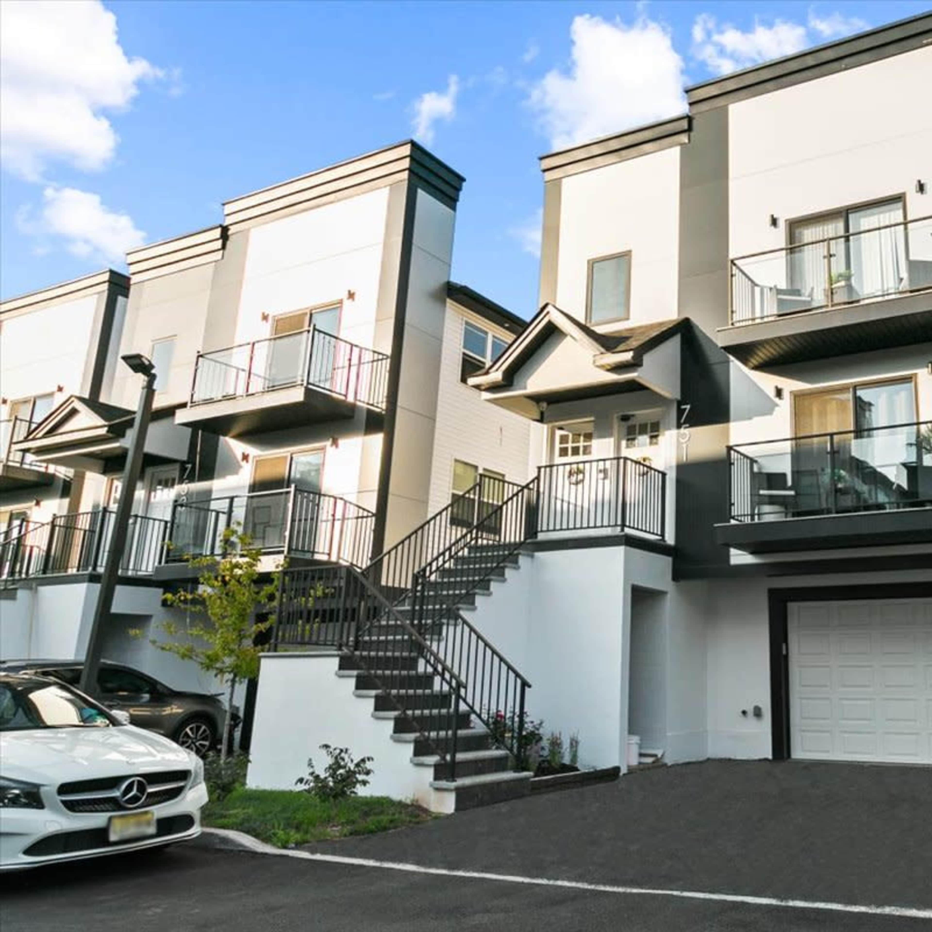 A modern multi-story townhouse with balconies and a garage, situated next to similar buildings in a residential area.
